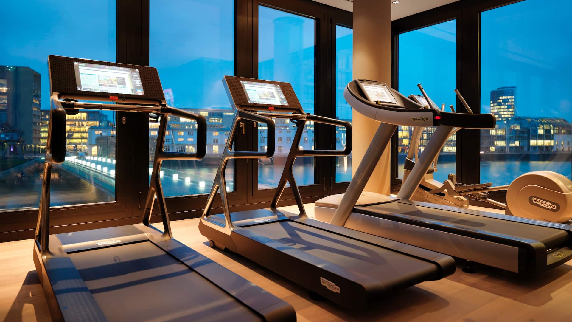 Spacious fitness studio at Hyatt Regency Dusseldorf with modern equipment treadmill, stepper and stunning MediaHarbor views
