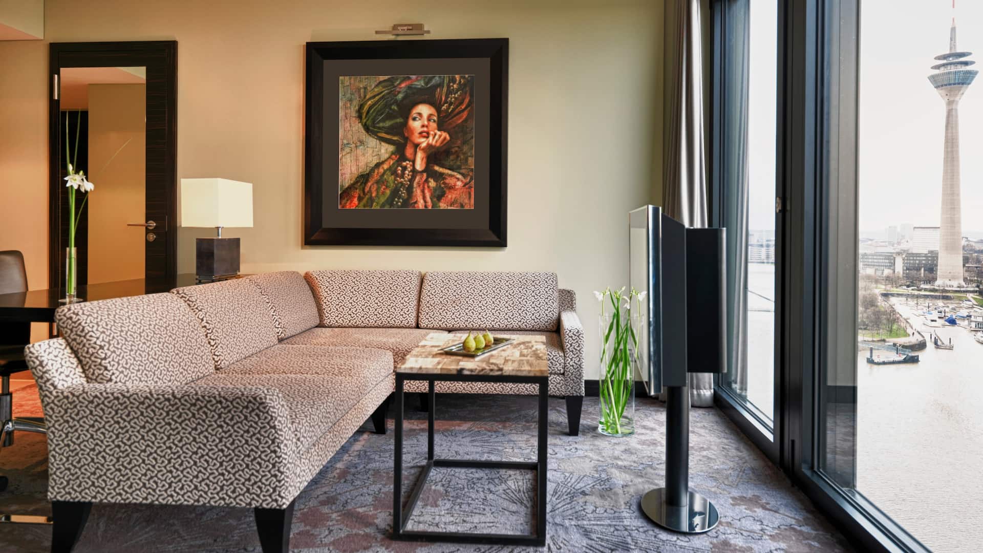 Regency Suite Wohn room at the Hyatt Regency Dusseldorf, with brown fabric corner couch, TV, floor to ceiling windows and view of the TV tower