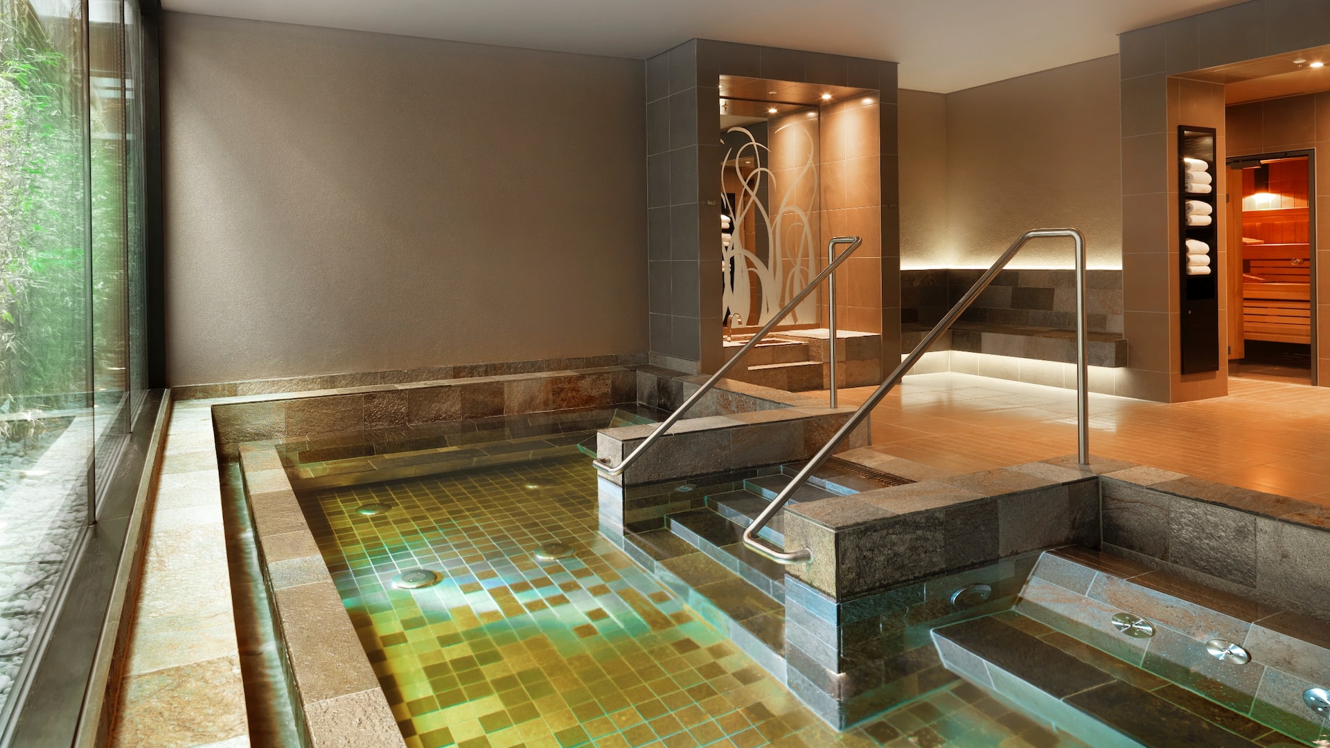 Rive Spa at the Hyatt Regency Dusseldorf, with large whirlpool that has green yellow tiles and sauna area in modern warm tone