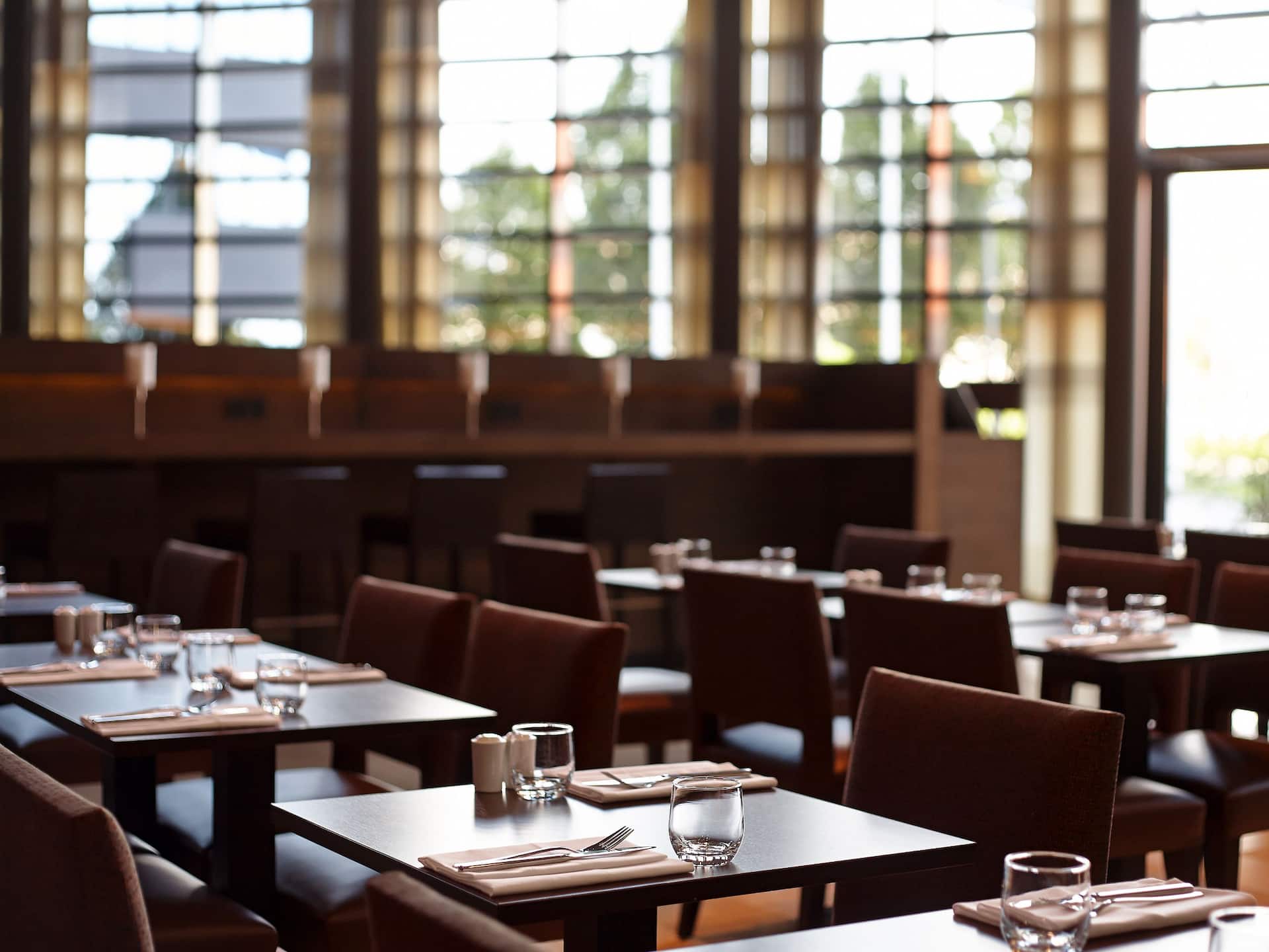 The dining area at Hyatt Place Amsterdam Airport, with well-arranged tables, glassware, utensils and large windows letting in natural light, and a modern, cozy ambiance.