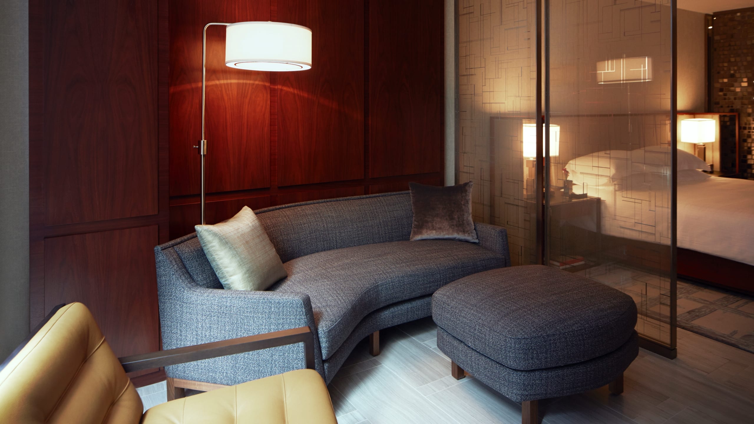 4 из 4 Suite living area with an armchair and couch with ottoman and screen with a king bed on the other side