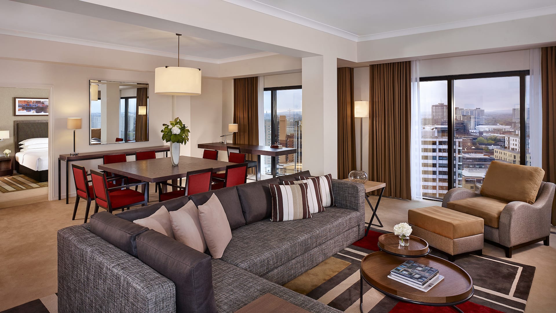 Spacious and comfortable Executive Suite living room with an L-shaped grey sofa, a chair and a dining room with a large wooden table at Hyatt Regency Birmingham.