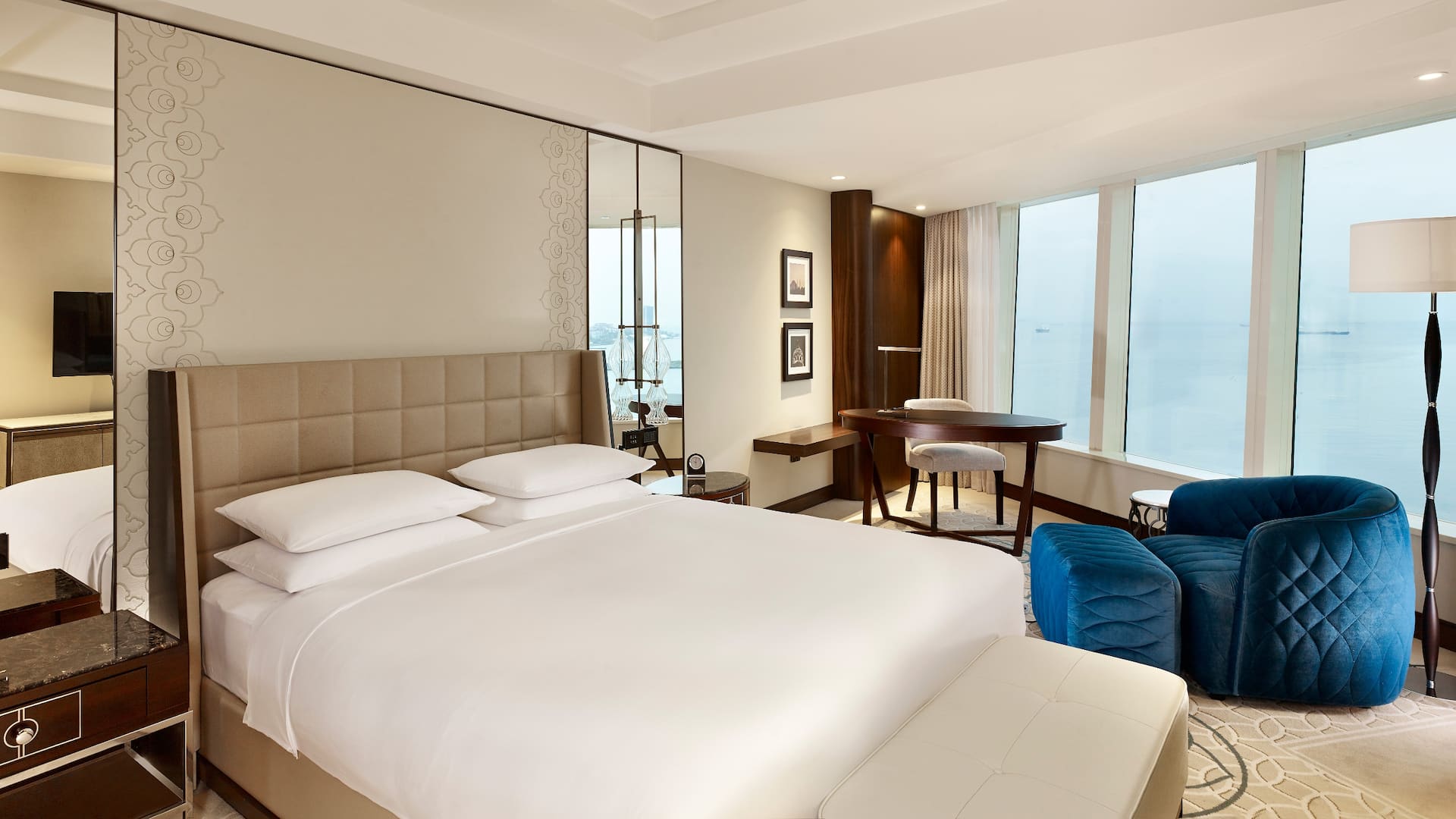 1 King Bed with Sea View at Hyatt Regency Istanbul Ataköy, featuring a tufted beige headboard, plush blue armchair, and large windows overlooking the sea.