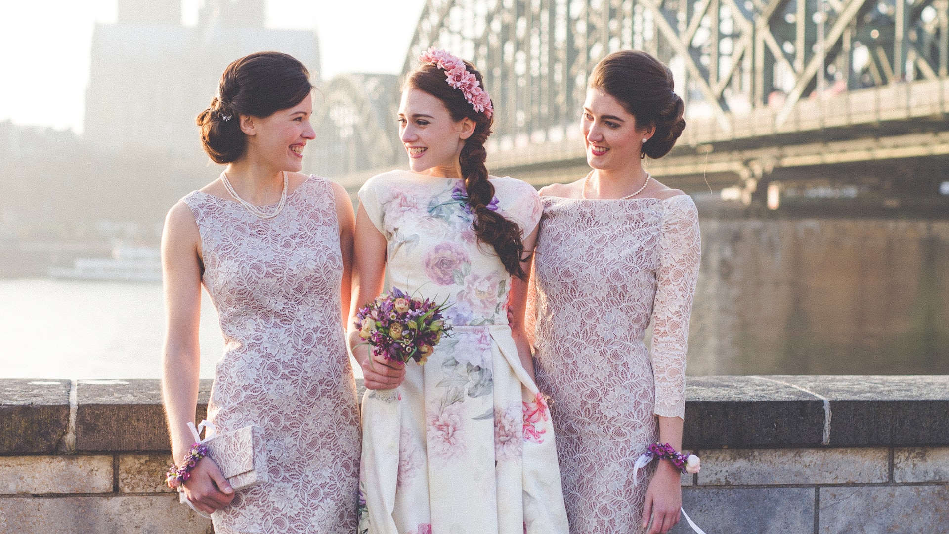 Bride with two bridesmaids in front of Hyatt Regency Cologne in floral dresses with the Hohenzollern Bridge in the back