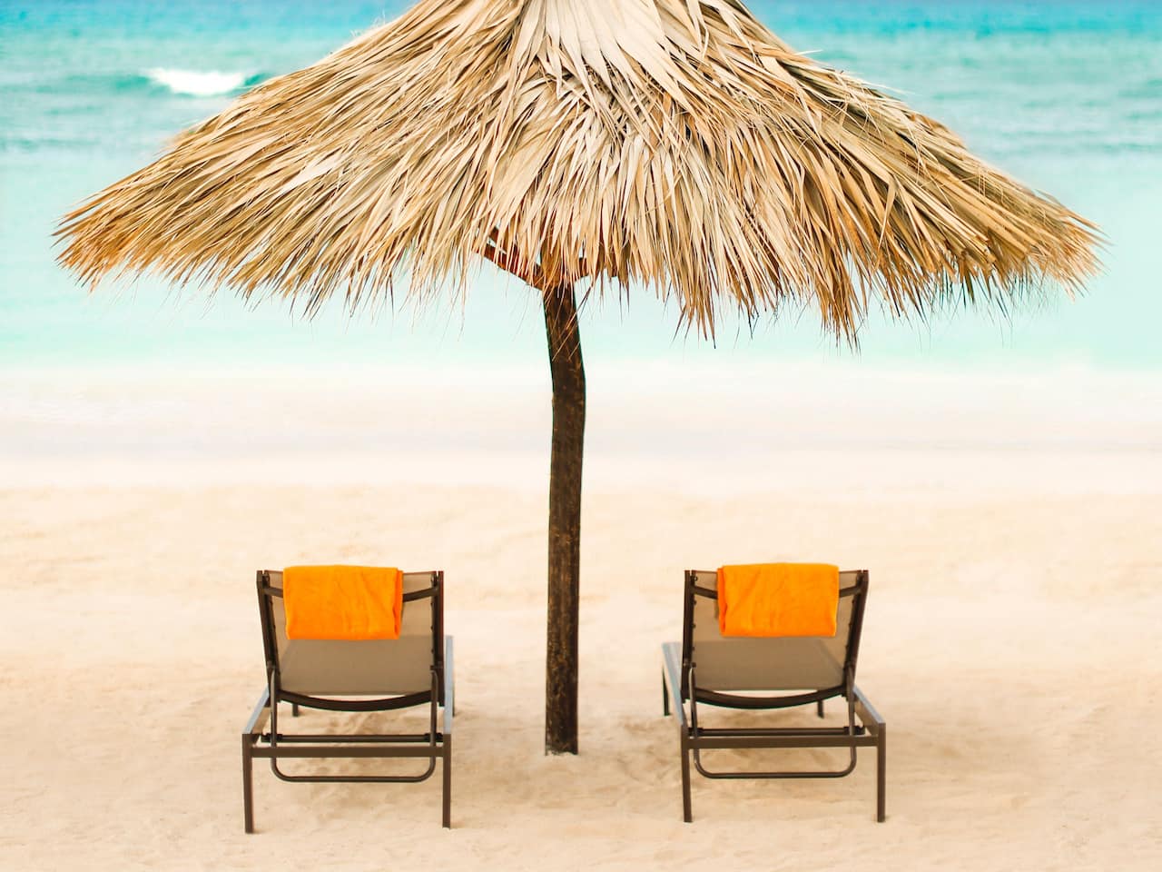 Two beach chairs under palm umbrella