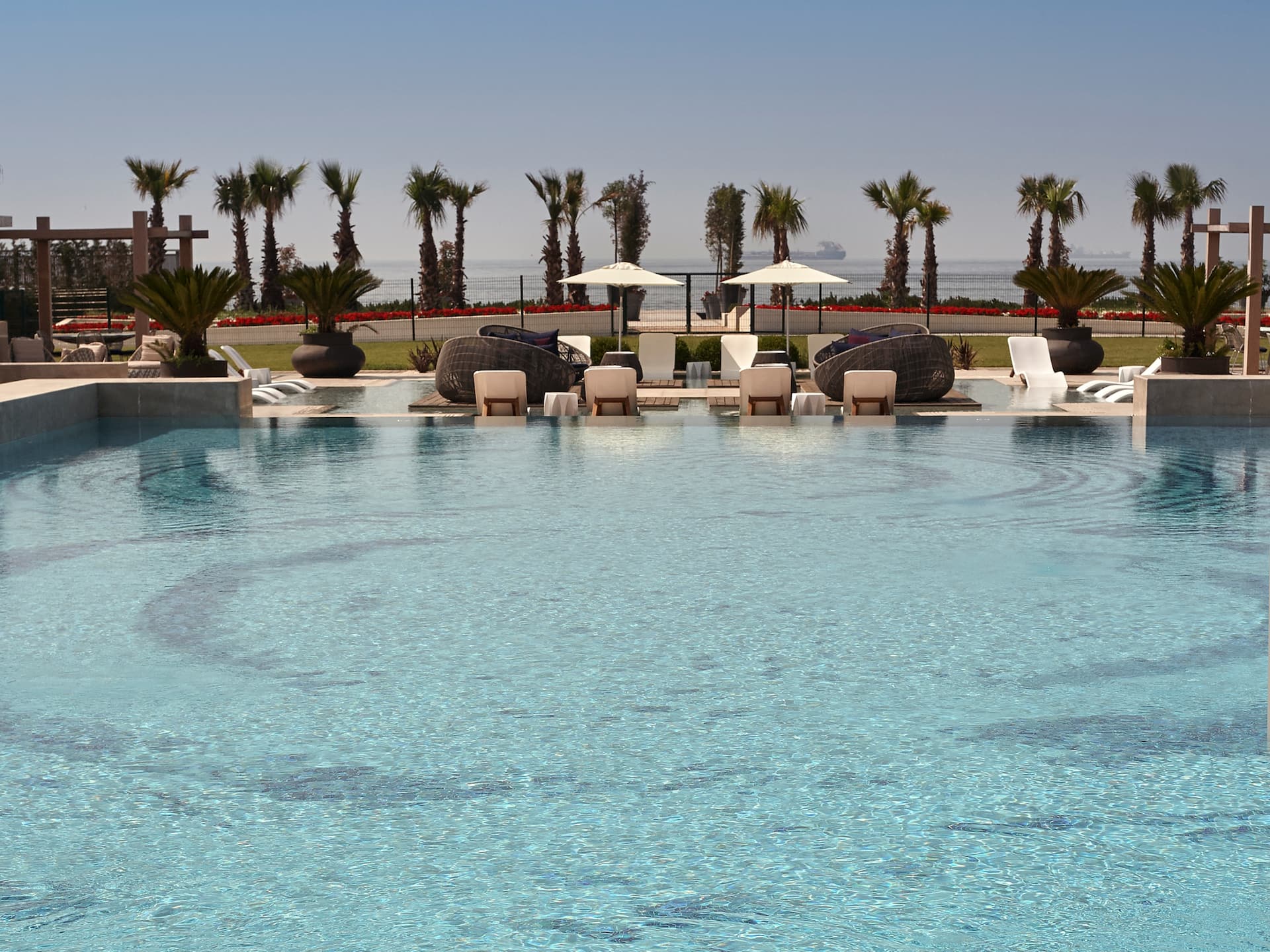 Infinity pool at Hyatt Regency Istanbul Ataköy with submerged lounge chairs, palm trees, and a sea view in the background.