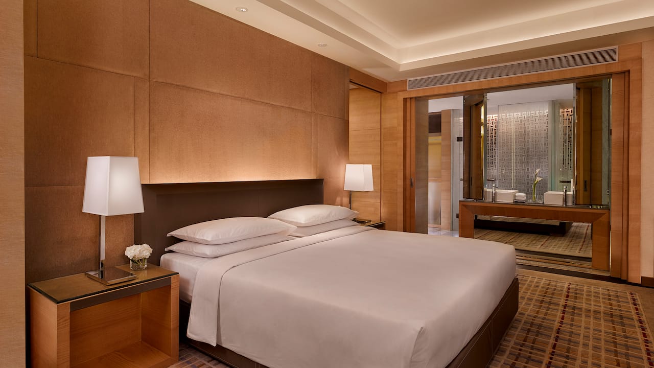King sized bed between nightstands with lamps by window in hotel room