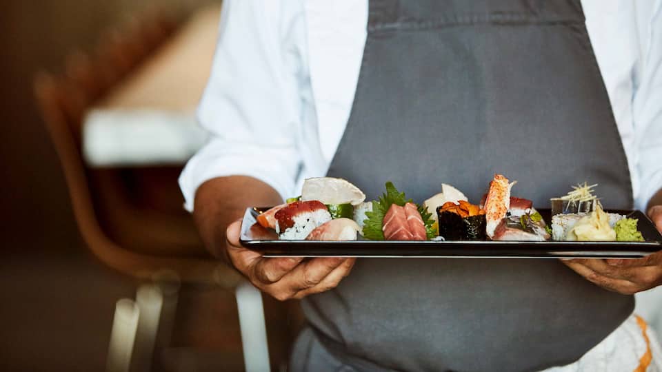 Hands Serving a Plate of Sushi