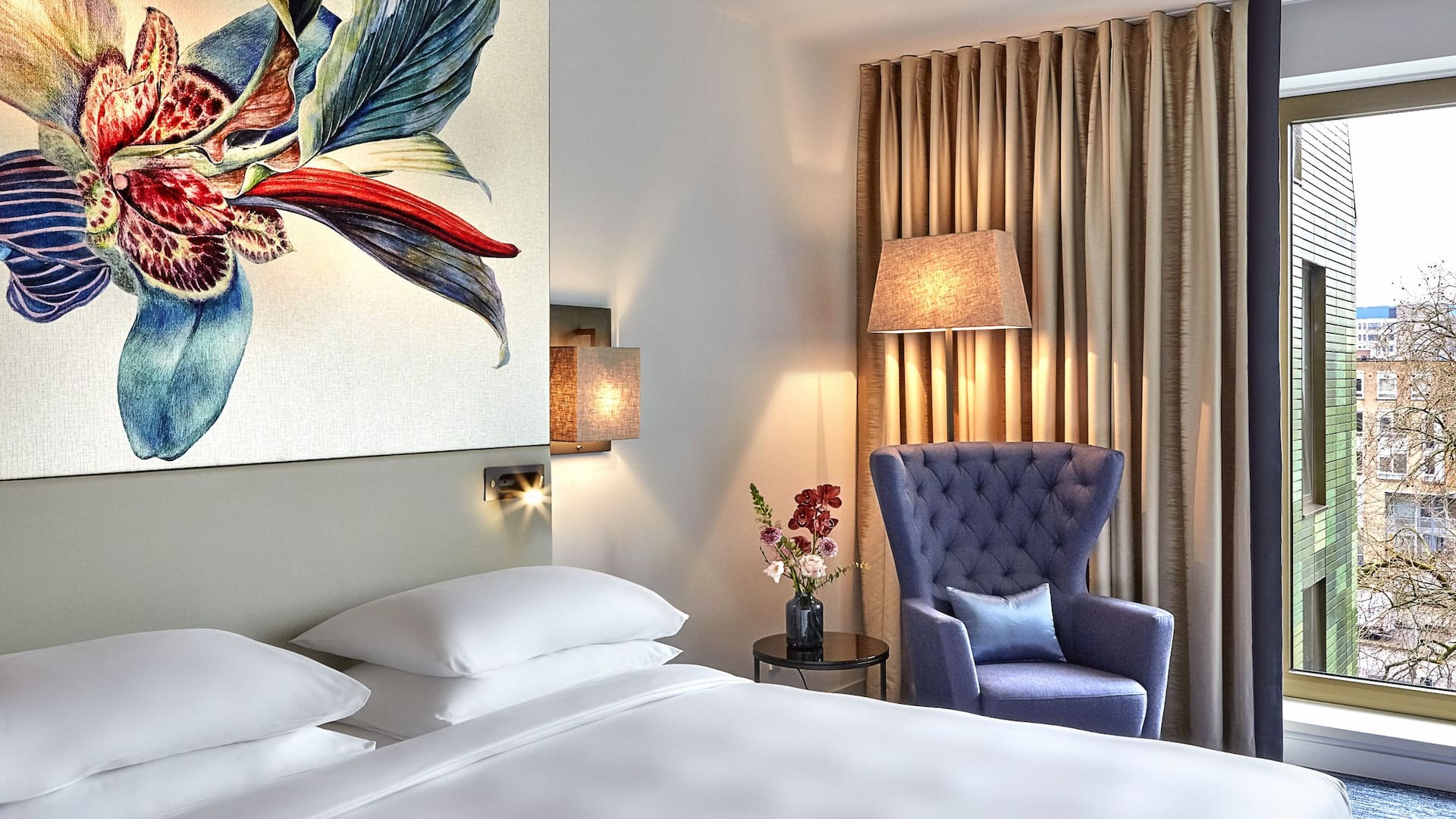 1 von 7 Amsterdam's hotel room with a view of the city, bed, a botanical headboard and a blue upholstered chair.