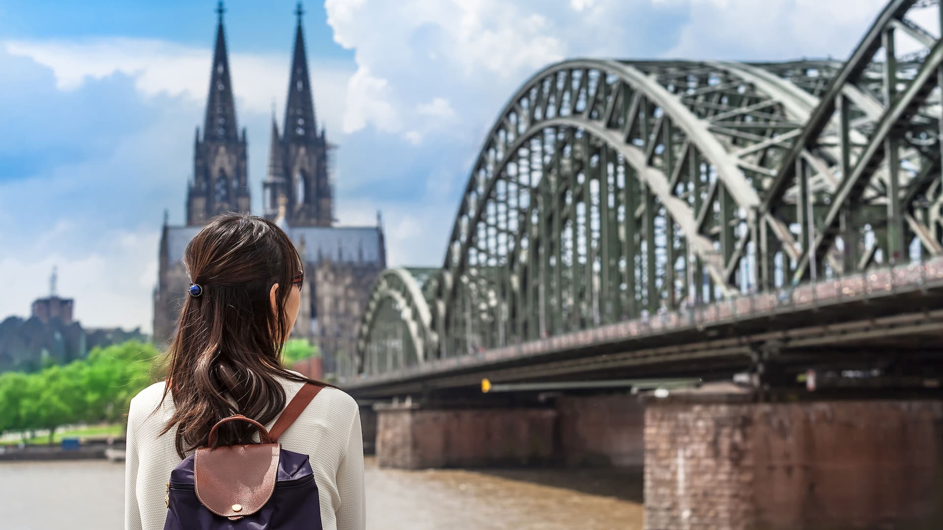 Woman standing on Rhine promenade near Hyatt Regency Cologne and looking at cathedral and Hohenzollern Bridge