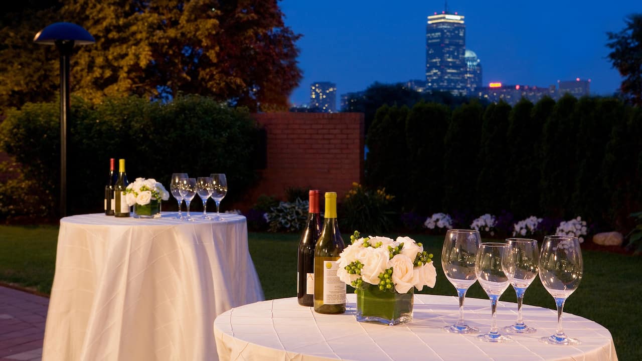 Tables with white table arrangements and wine set outside with a view of Boston