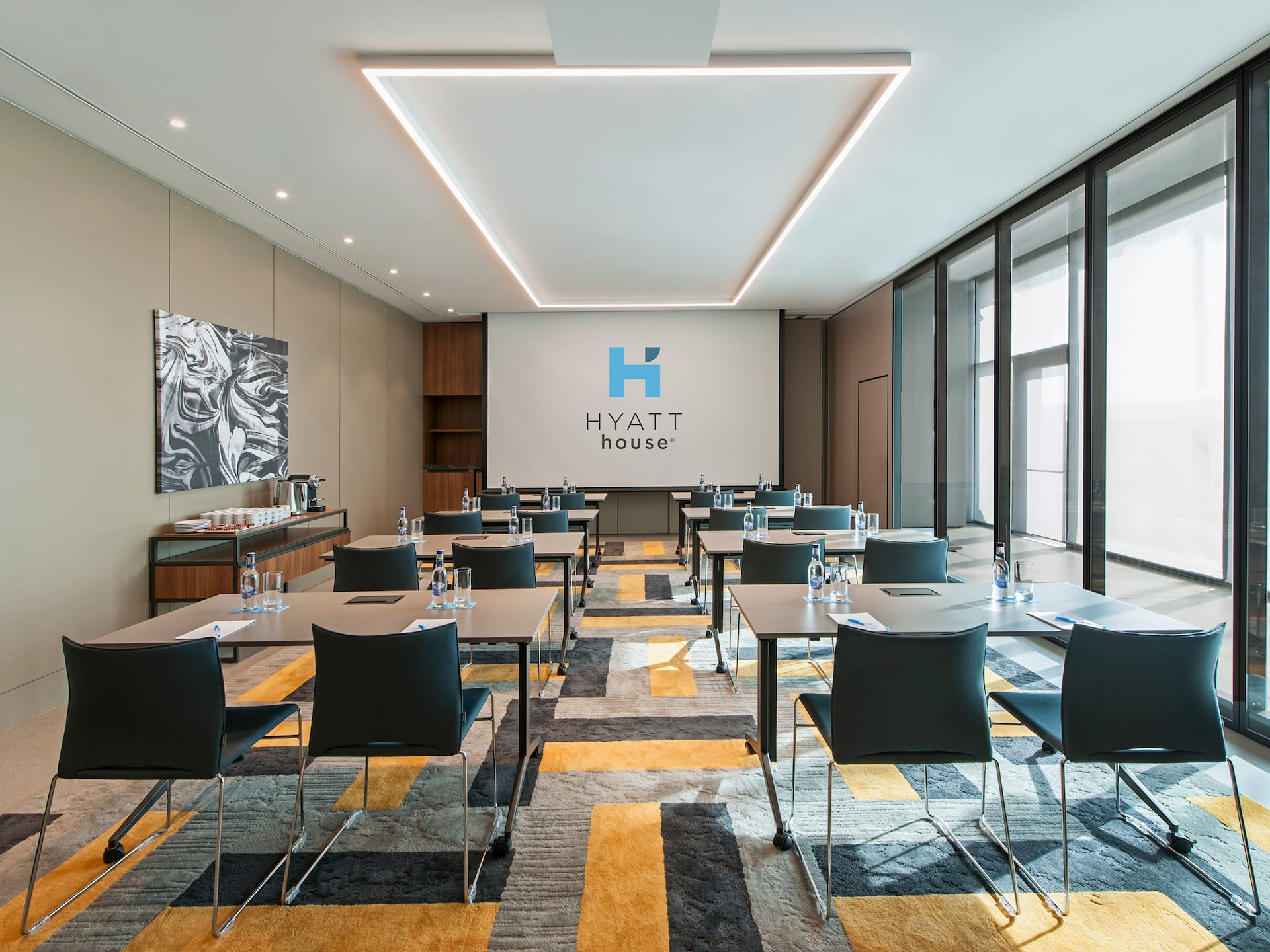 Meeting venue in Gebze with a high ceiling, classroom layout, sunlit windows, colorful carpet, and large screen at Hyatt House Gebze, ideal for corporate events and conferences