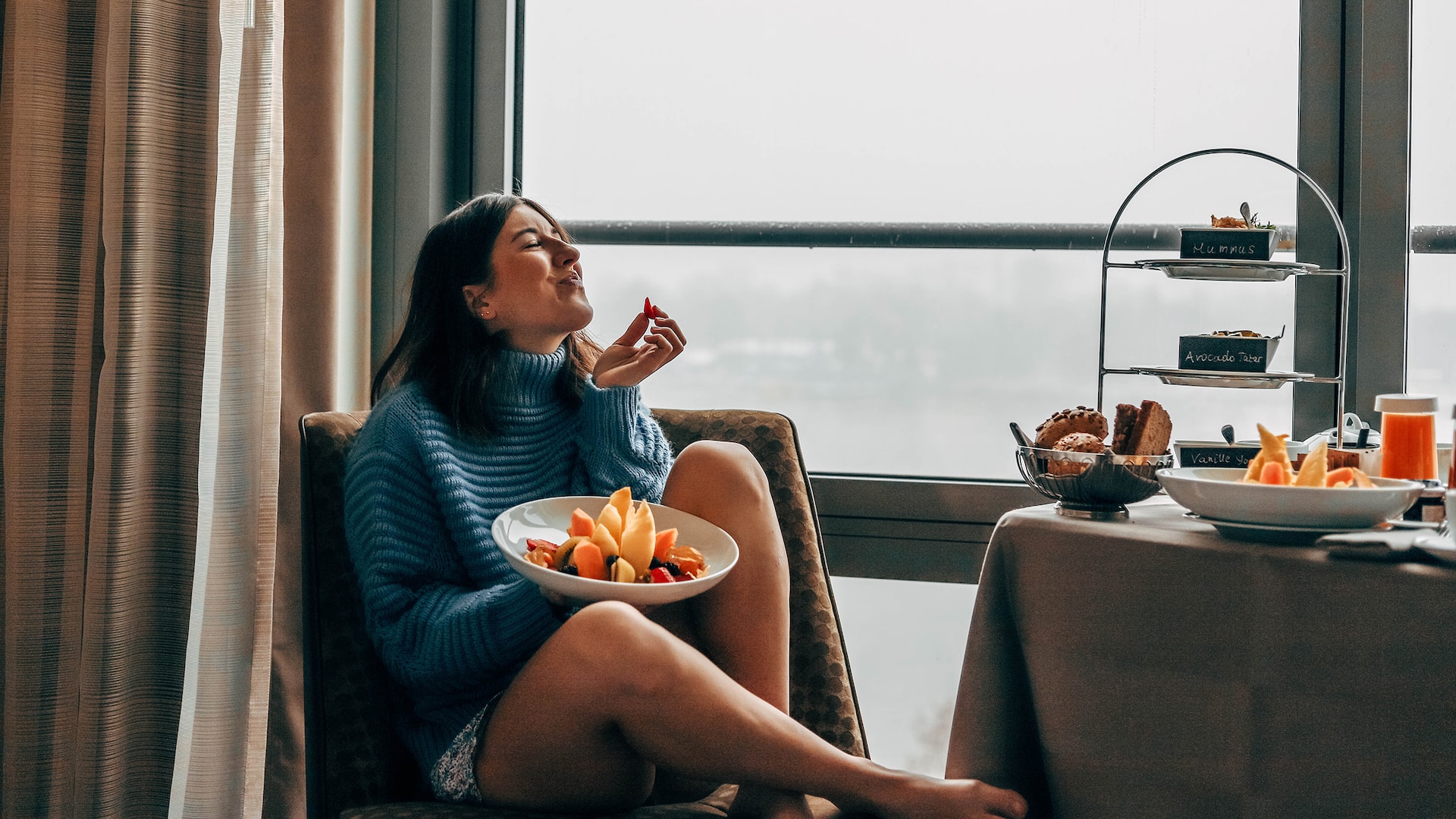 2 de 6 Ein weiblicher Gast sitzt vor dem Fenster eines Rheinblickzimmers im Hyatt Regency Mainz Hotel und genießt ihr Room Service Frühstück.