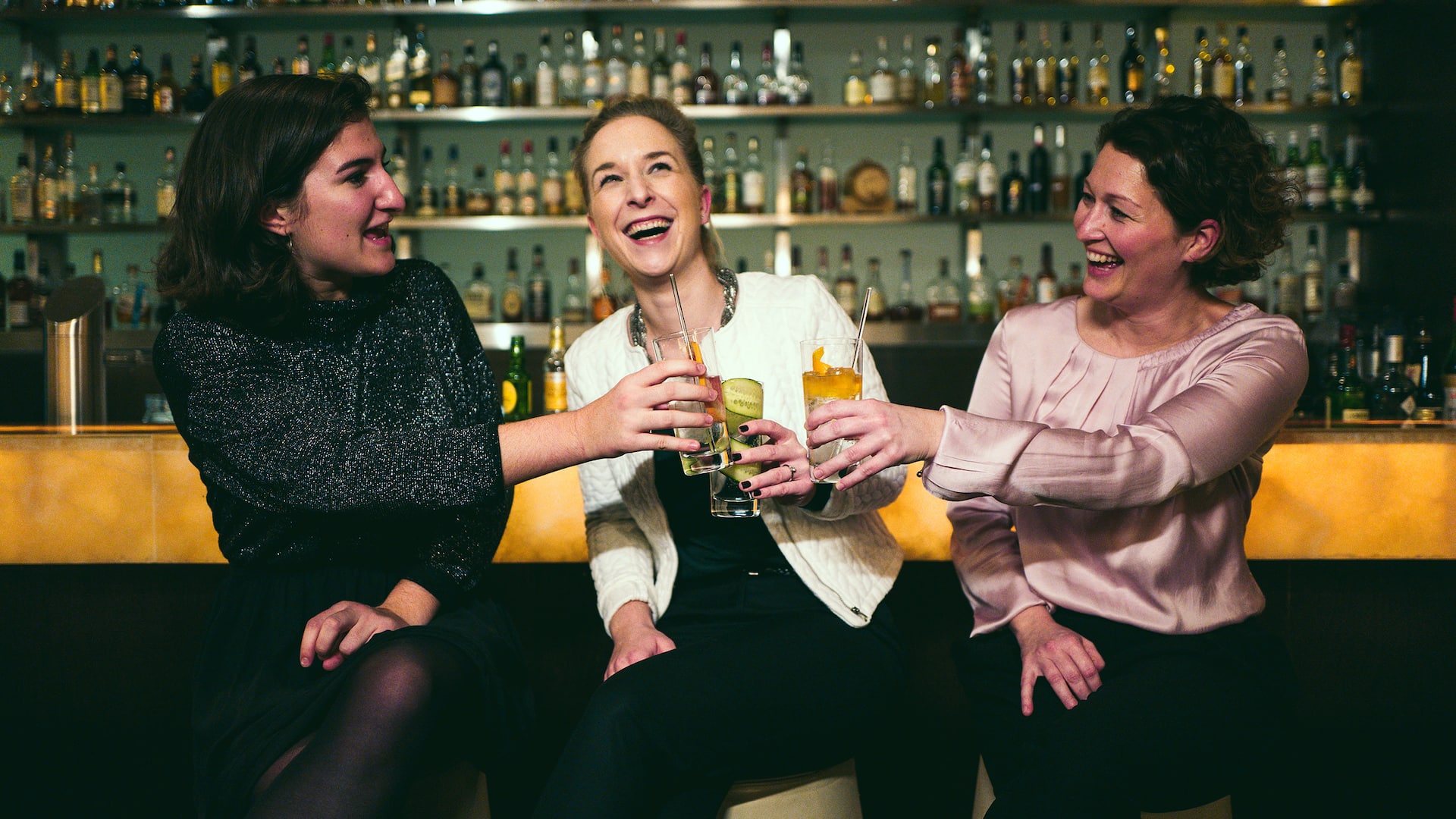 Three laughing women toast each other at the bar of the Vox Bar at Grand Hyatt Berlin