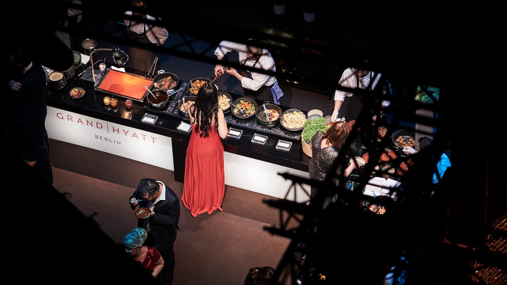 Frau in rotem Abendkleid steht an Büffet und wird bedient - Hyatt Catering Berlin