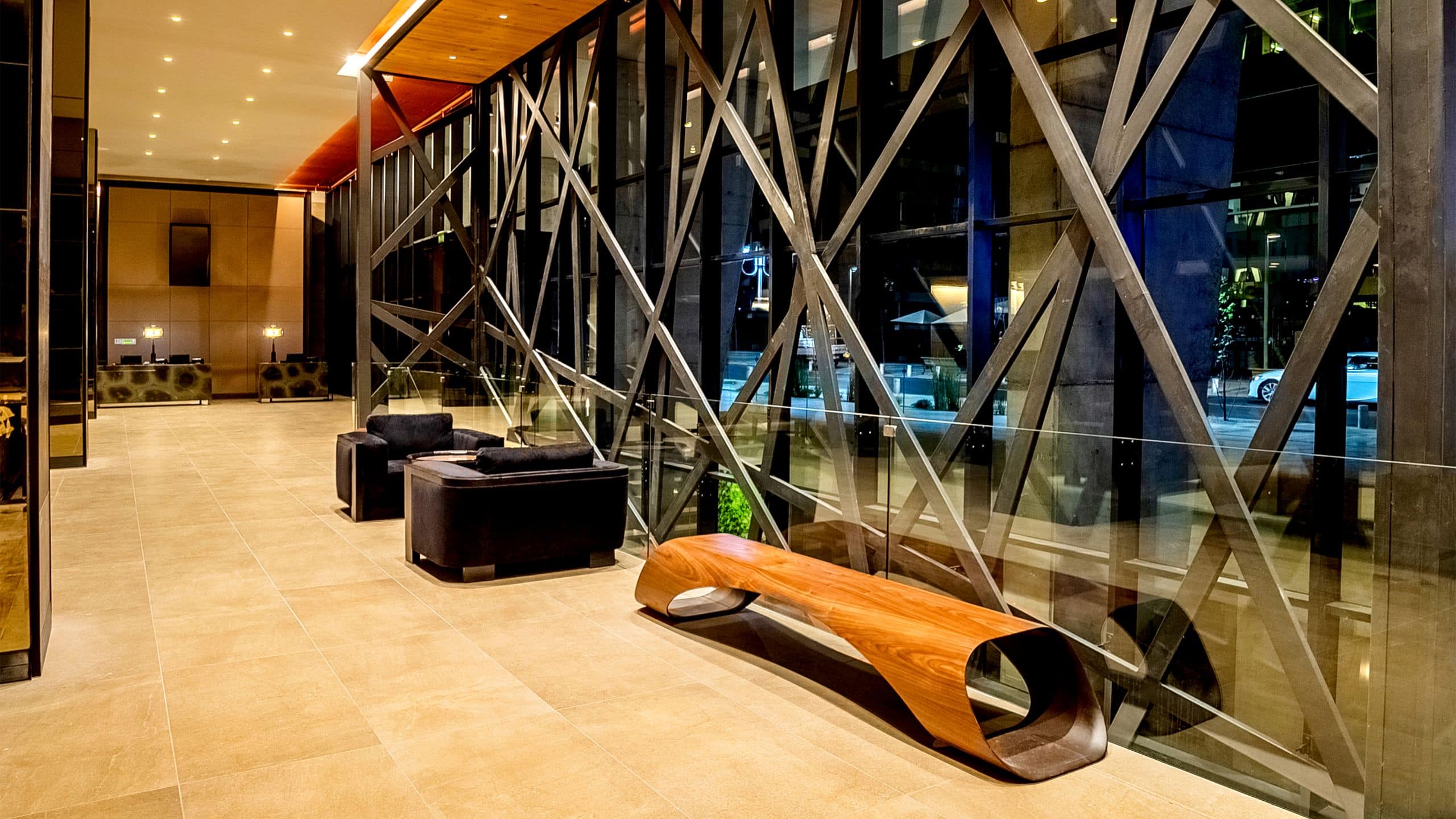 Hotel entryway with floor to ceiling windows, modern bench and leather chairs