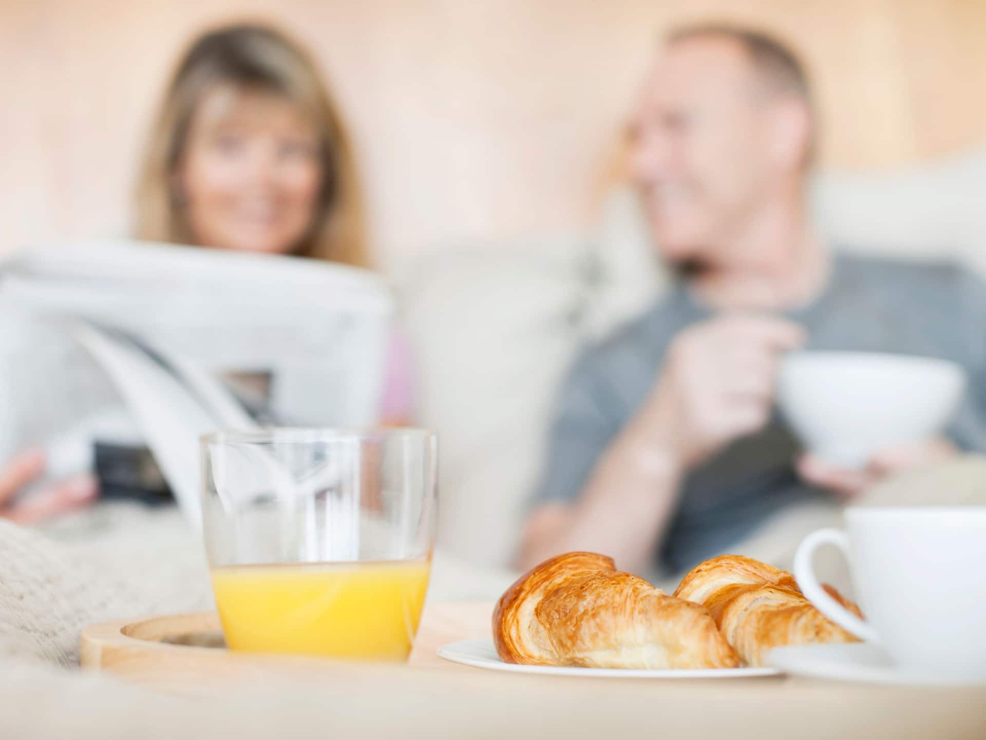 Room Service photo featuring a couple on the bed reading a newspaper while having coffee, juice and pastries.