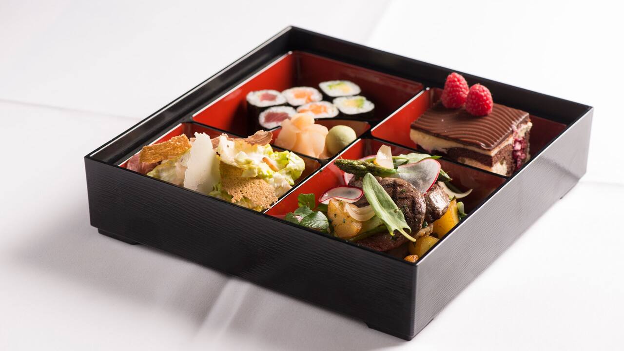 Filled bento box with sushi, Cesar salad, meat and vegetables and chocolate cake