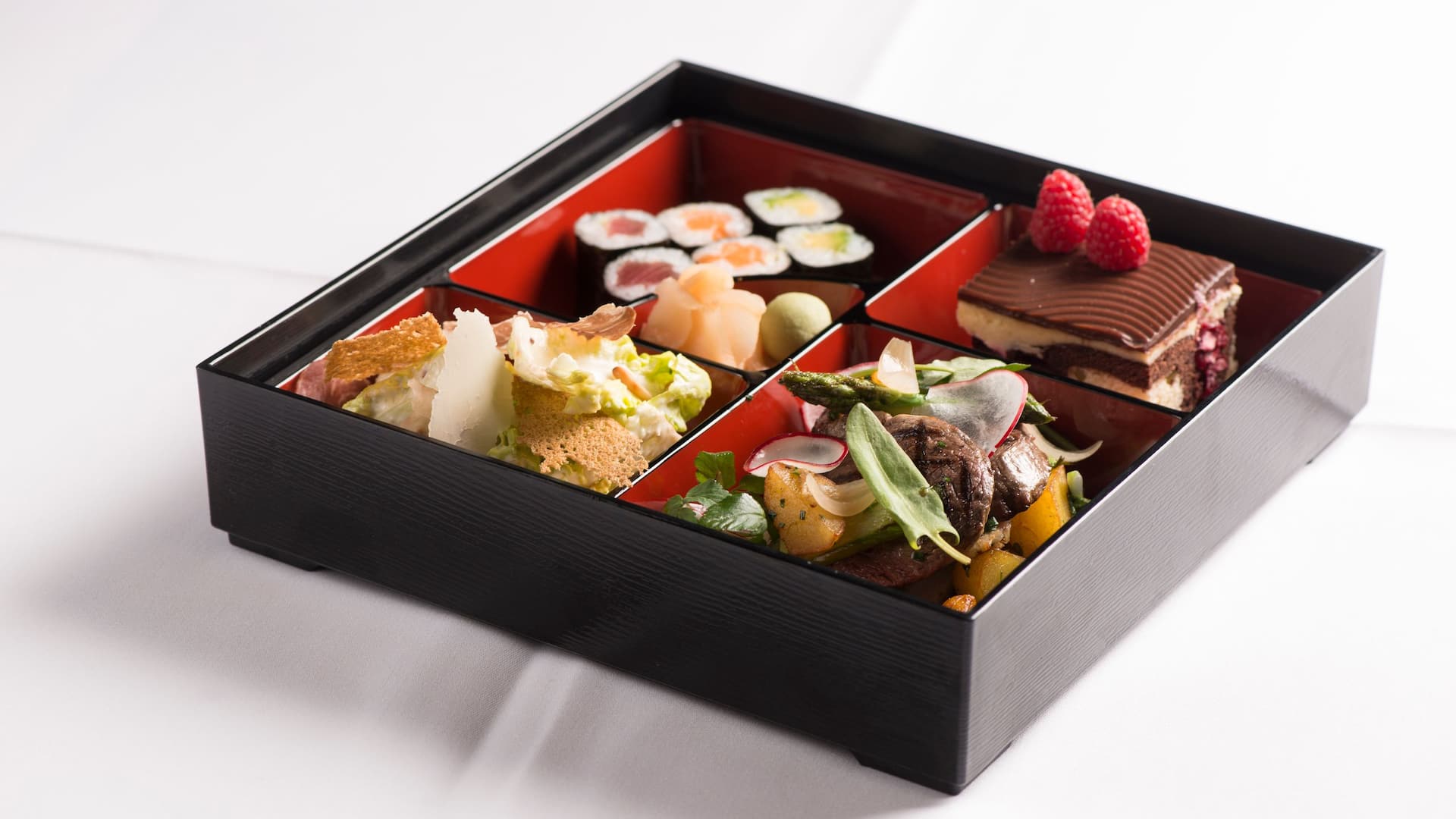 Gefüllte Bento Box mit Sushi, Cesar Salad, Fleisch und Gemüse sowie Schokoküchlein 