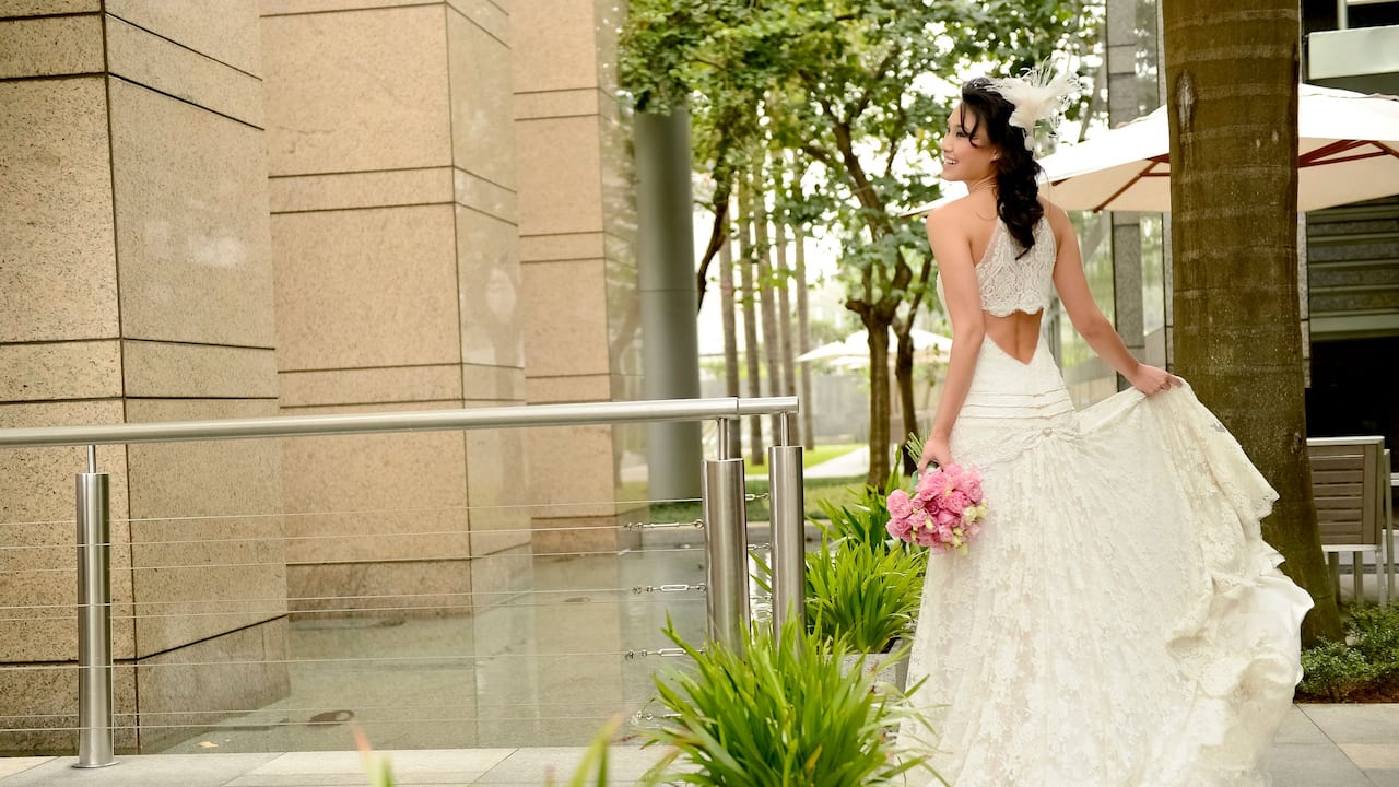 Bride with wedding bouquet posing for a photo with a fountain and trees in the background