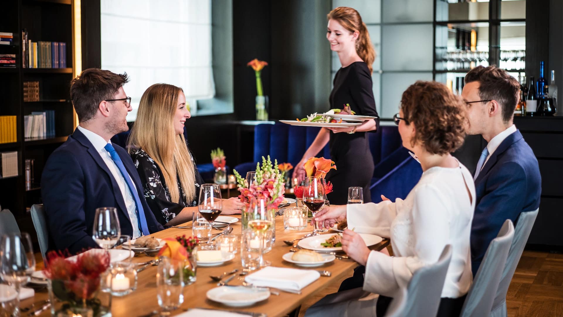 People sit at a table in the library of Grand Hyatt Berlin and are served dinner