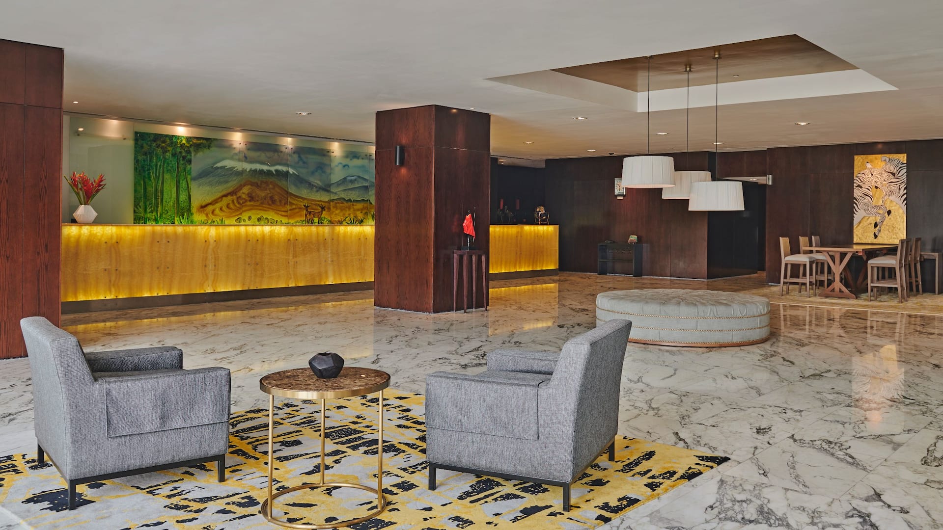 Interior of the hotel lobby, showcasing an elegant setup with rich background tones at the reception desk, featuring a drawing of Mount Kilimanjaro behind the receptionists.
