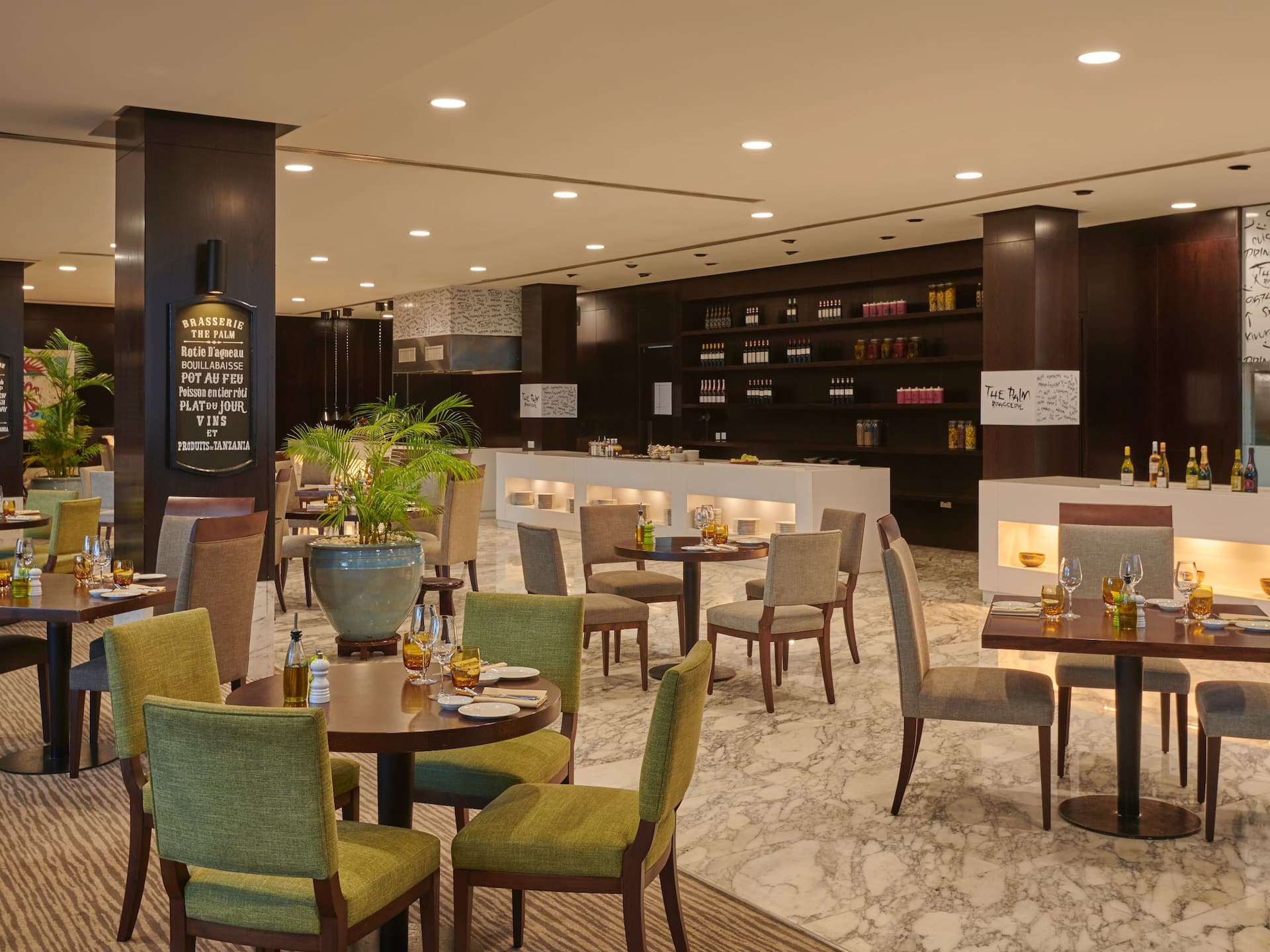 Interior of The Palm Brasserie on the ground floor of Hyatt Regency, featuring a stylish arrangement of tables and chairs with green, blue, and muted color tones in the décor