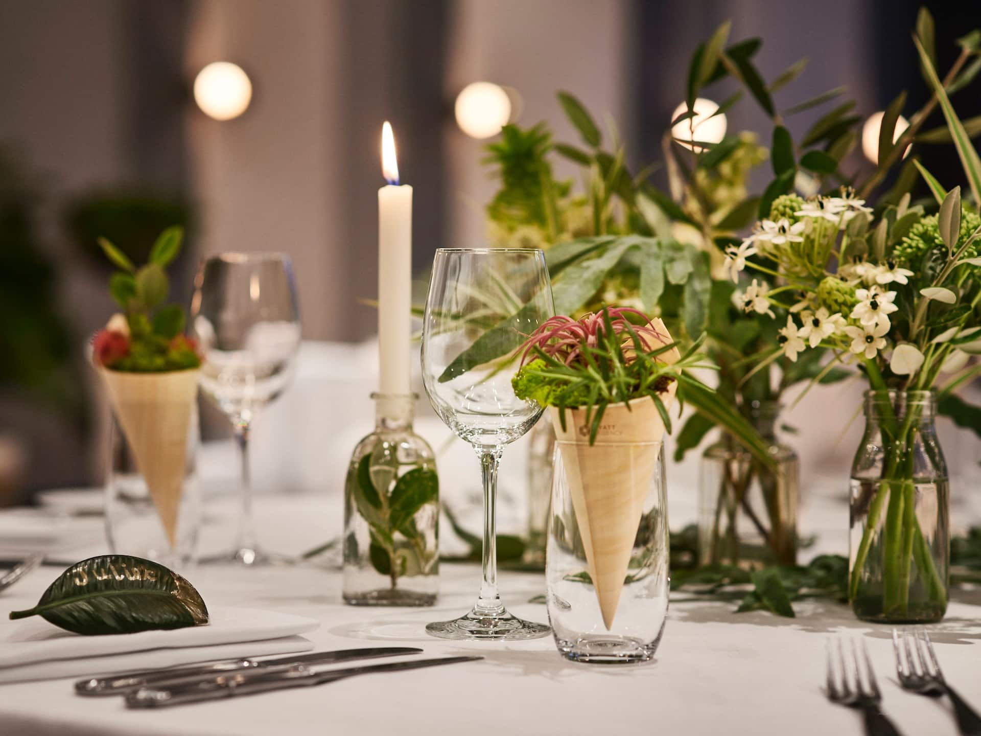 A closer-up of a dinner setup at Hyatt Regency Amsterdam, with arranged cuttly, a candle, and small plants on the table.