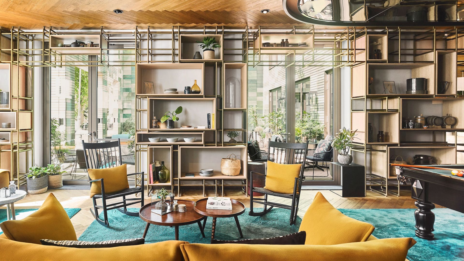 Amsterdam Bar Lounge Seating at Hyatt Regency Amsterdam, with yellow chairs, a turquoise rug, and a modern shelving unit with plants.