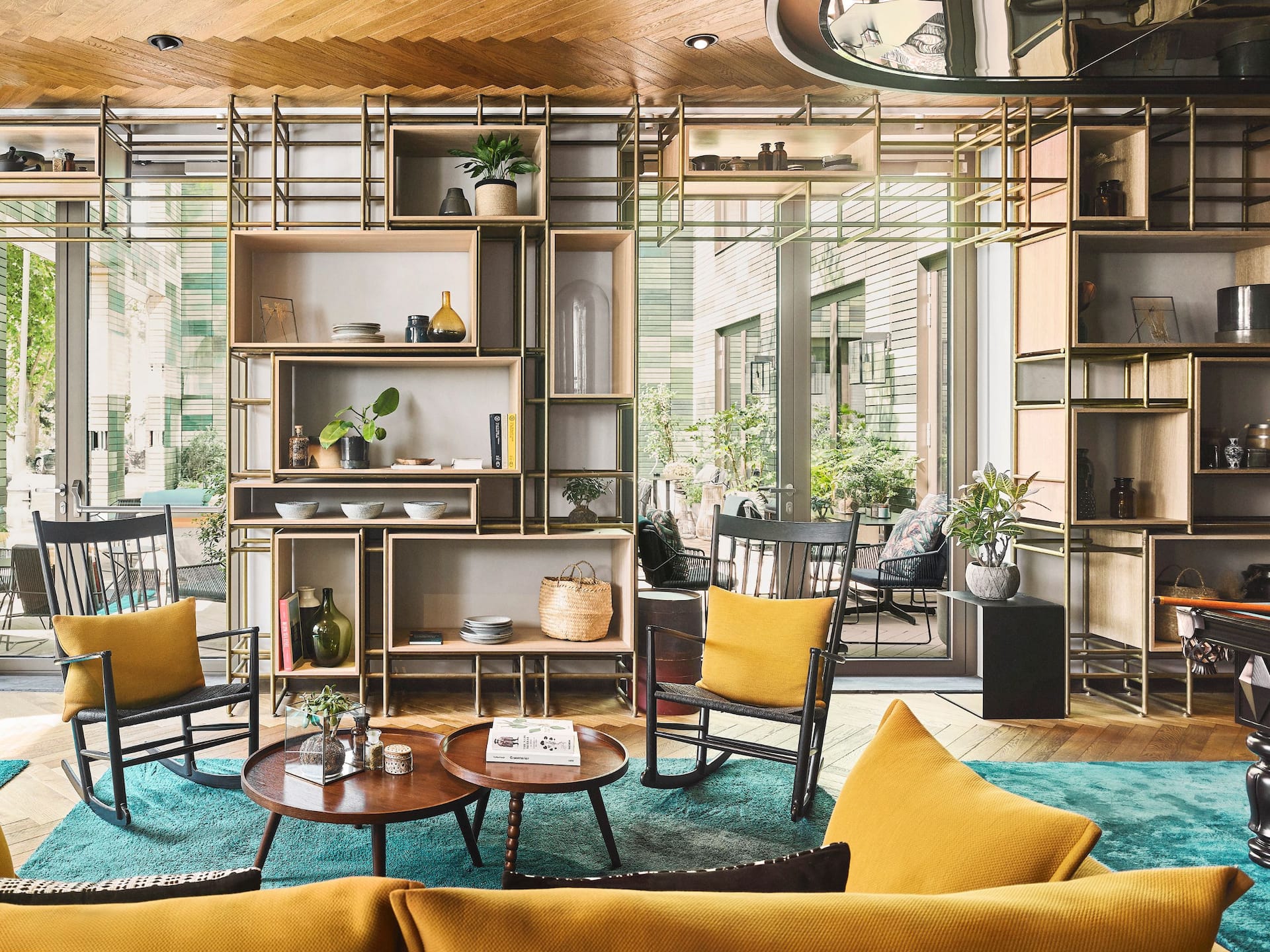 Amsterdam Bar Lounge Seating, A public space at Hyatt Regency Amsterdam, with yellow chairs, a turquoise rug, and a modern shelving unit with plants.