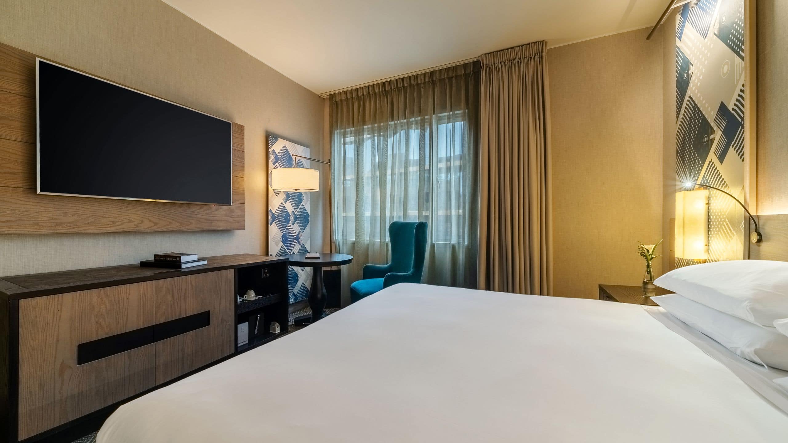 1/1 One King Bed guest room with wall mounted television, small work table and reading chair