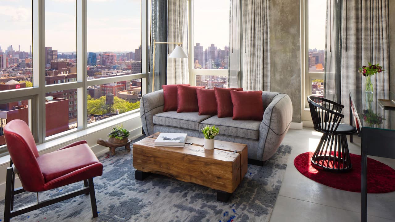 Bowery Suite living room with sofa, wood coffee table, and floor-to-ceiling windows with city views