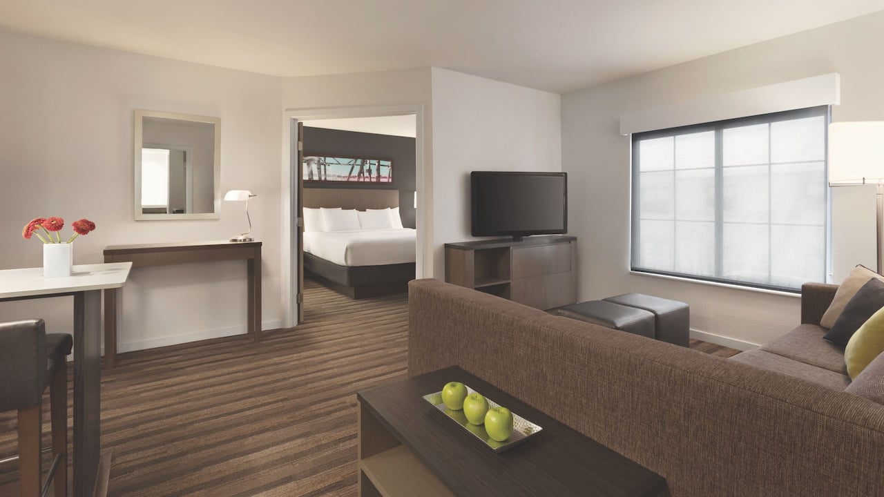 Two-bedroom suite with open doorway to king size bed, living room sofa and tv at Hyatt House Boston / Burlington 