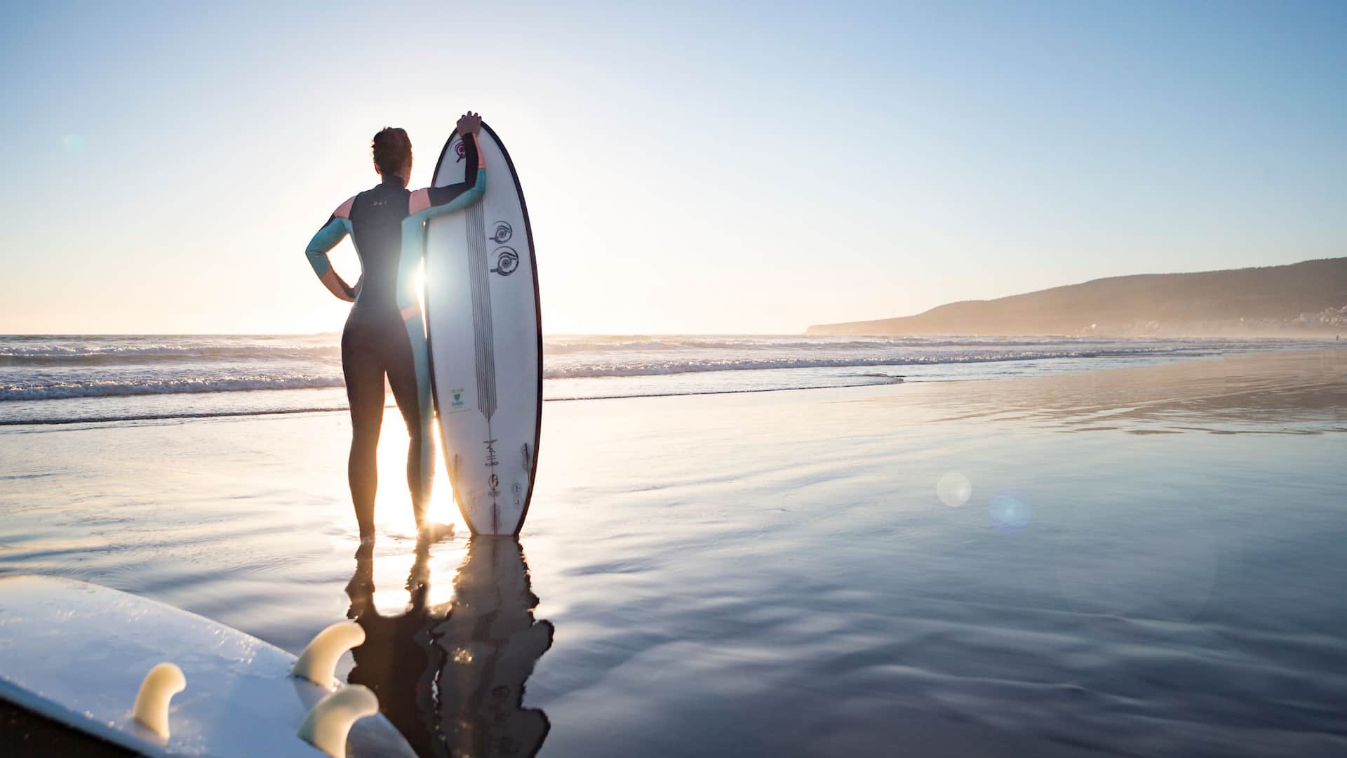 Girl holding her surfboard, looking out at the sea, ready to ride the waves