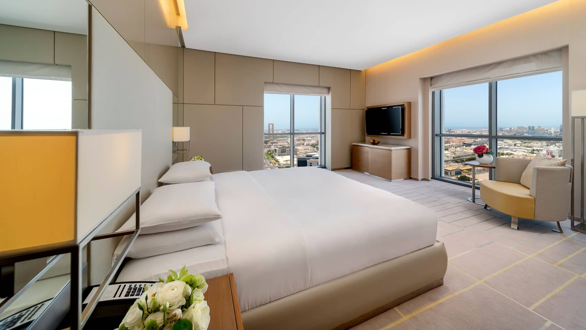A spacious suite with a king bed, natural daylight, and panoramic view of city skyline