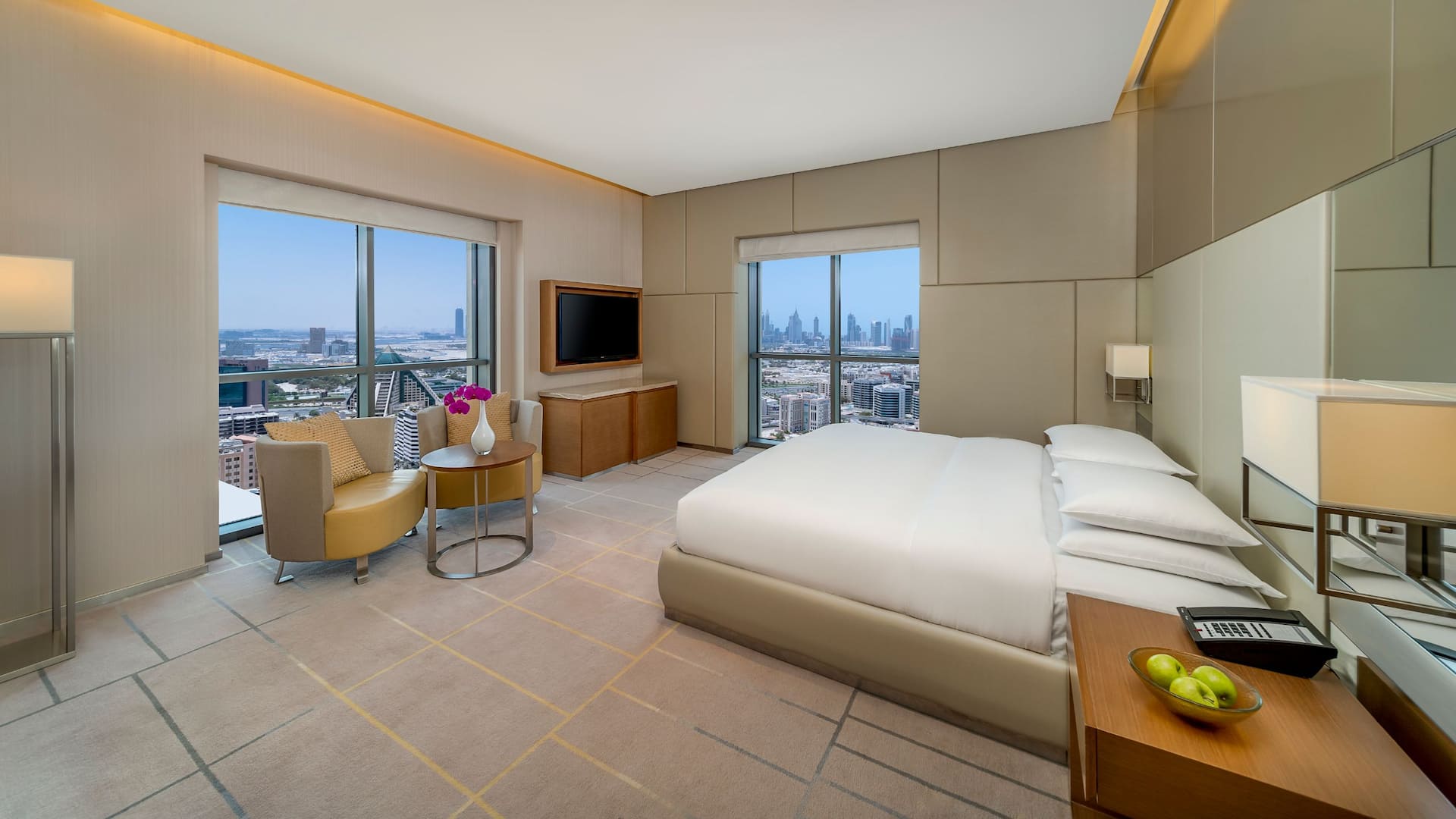 A suite with a king bed and comfortable seating space overlooking the city of Dubai.