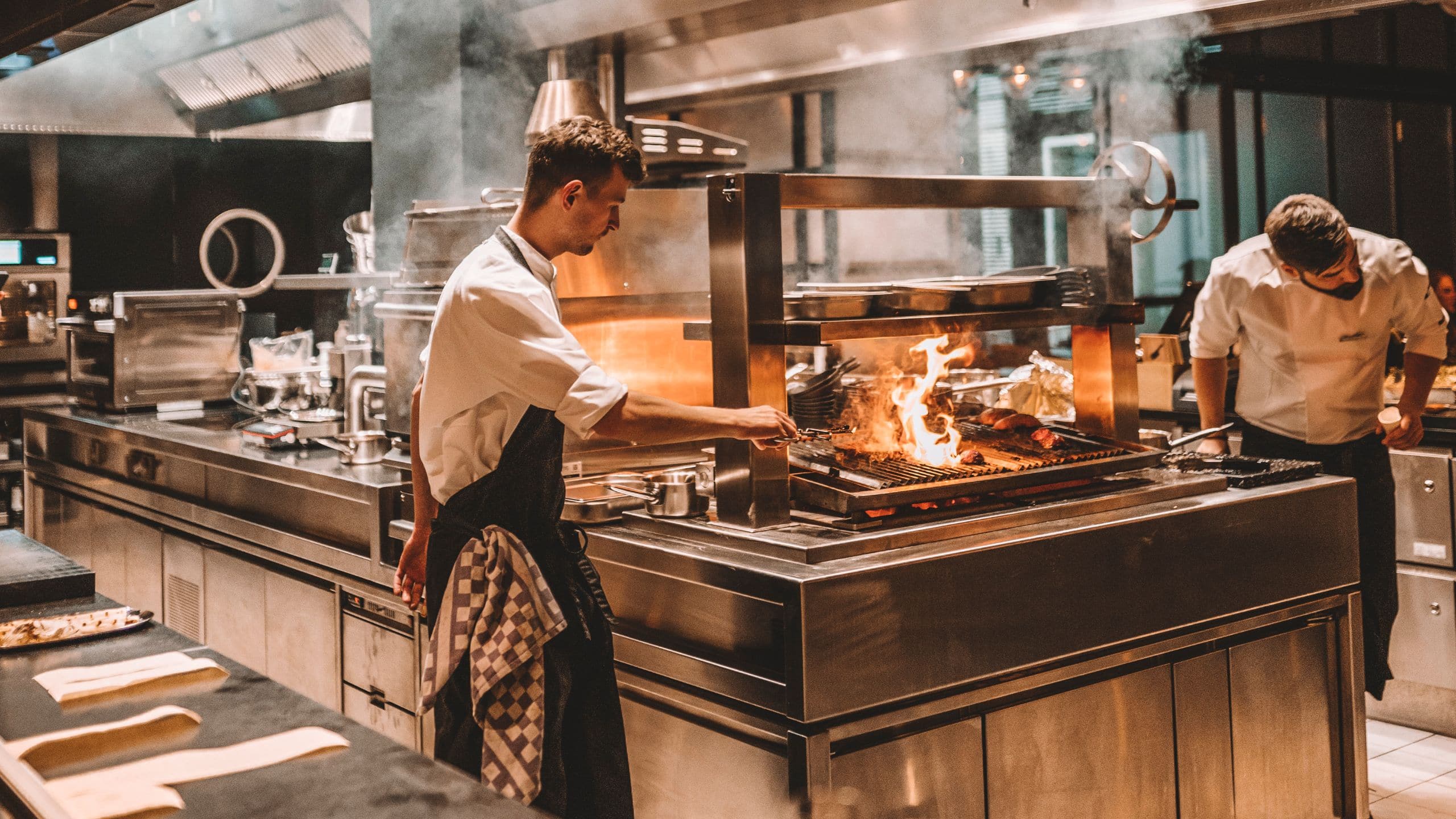 Open kitchen at The Lonely Broccoli restaurant, Andaz Munich, with chefs cooking over open flames in a lively atmosphere