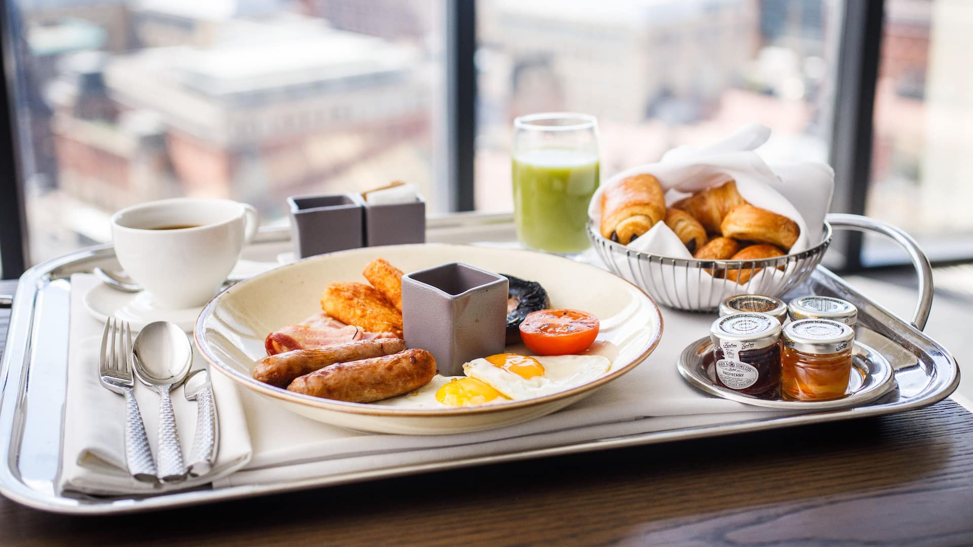 1 of 1 Tray on a wooden table with a classic breakfast composed of croissants, pain au chocolat, an English breakfast with eggs, beans, sausages and a coffee with a view of Birmingham.