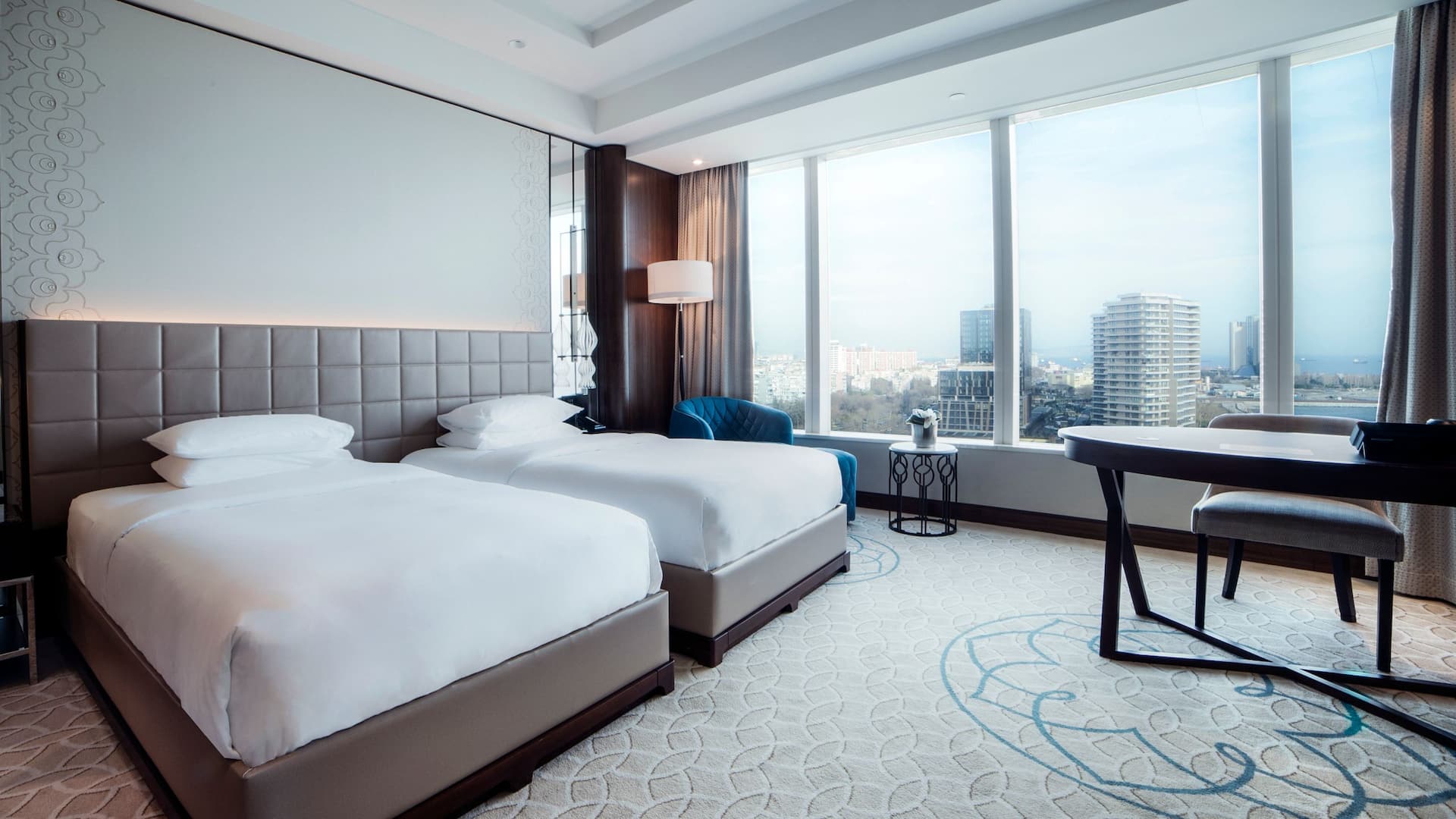 2 Twin Beds with Club Access at Hyatt Regency Istanbul Ataköy, featuring a tufted beige headboard, plush blue armchair, and panoramic city views.