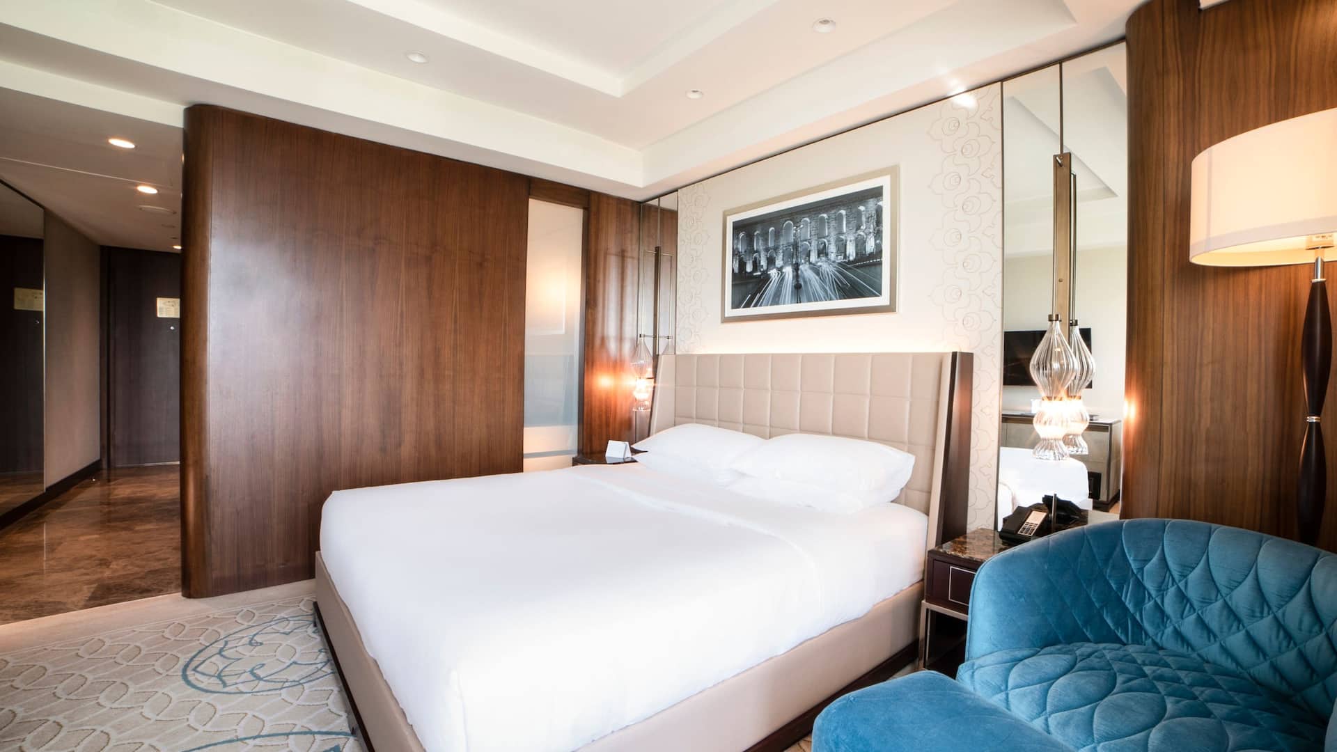 2 de 7 1 King Bed at Hyatt Regency Istanbul Ataköy with a tufted beige headboard, wooden accents, modern décor, and a plush blue armchair.