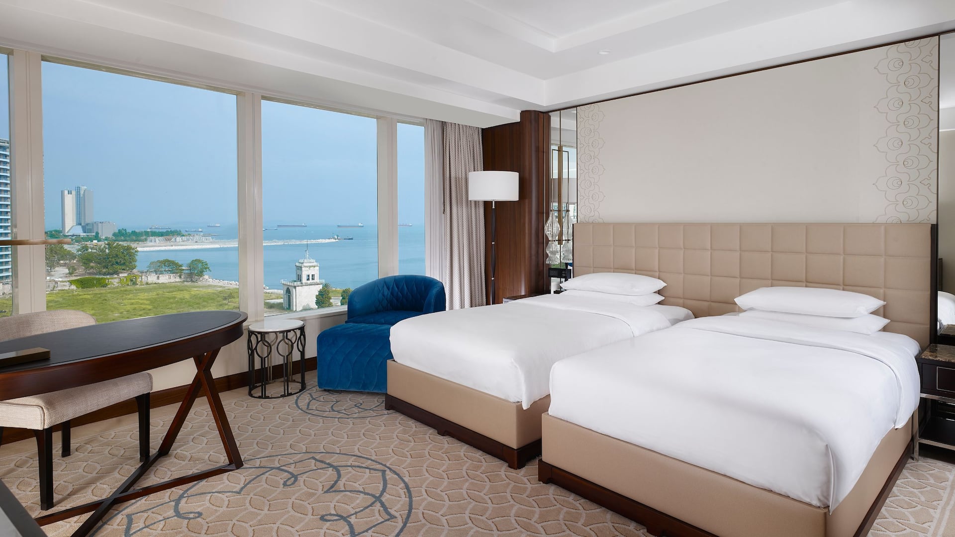 Twin Beds with Sea View at Hyatt Regency Istanbul Ataköy, featuring a tufted beige headboard, a plush blue armchair, large windows, and modern décor.