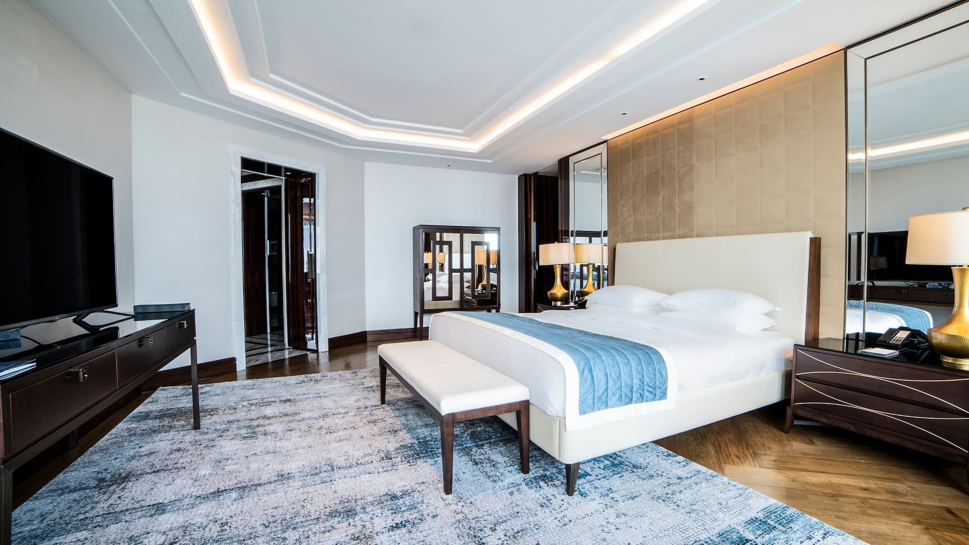 Spacious Diplomatic Suite at Hyatt Regency Istanbul Ataköy featuring a plush king-size bed with mirrored accents, gold-toned lamps, modern furniture, and a neutral color palette for a refined stay experienc