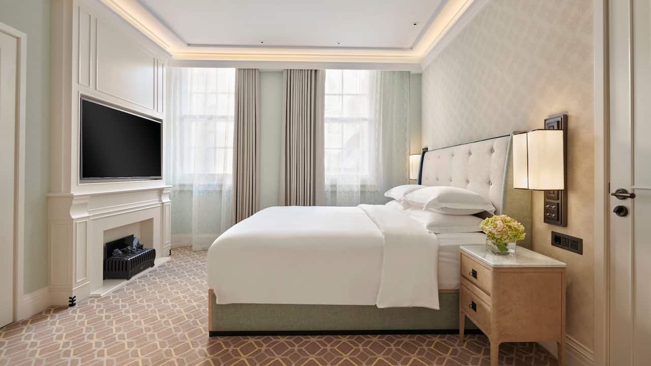 Hotel suite with king bed, bedside table and tv above the fireplace
