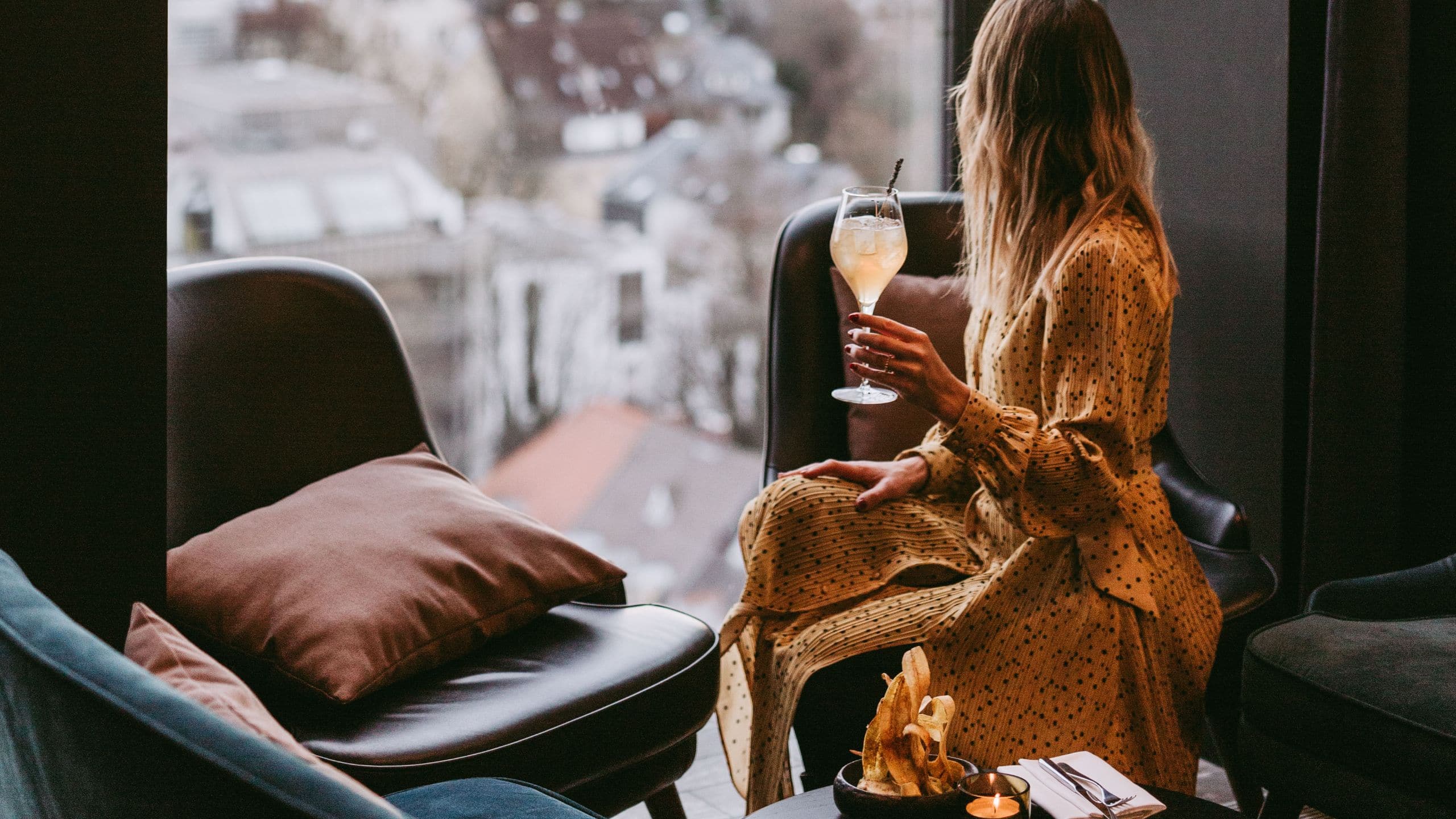 Woman enjoying cocktail while looking out of the floor to ceiling window of the modern M Uniqo rooftop bar with city views