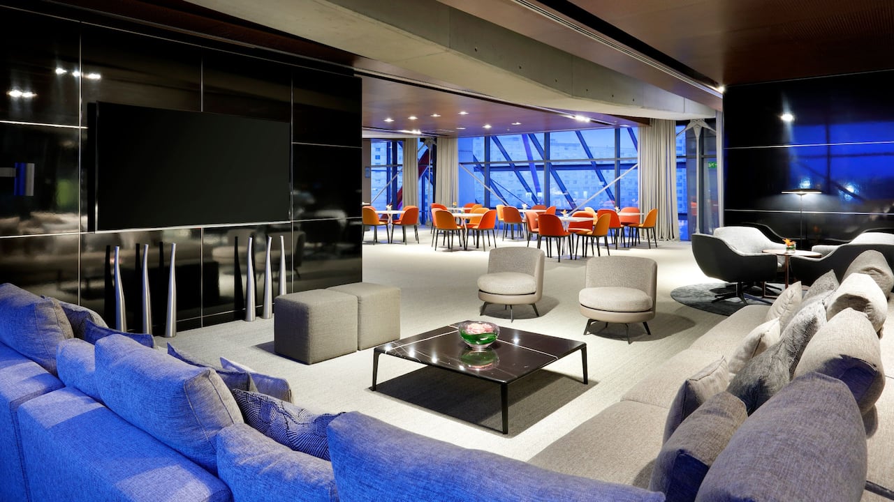 Common area with sofas, TV, and tables located in the Regency Club of our Hyatt Regency Barcelona Tower hotel.