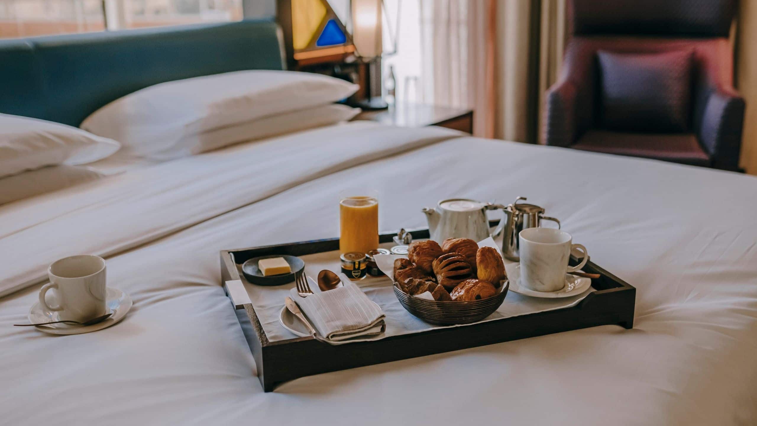 A breakfast tray with fresh juice and pastries served on the bed from in-room dining option at Andaz Dubai The Palm