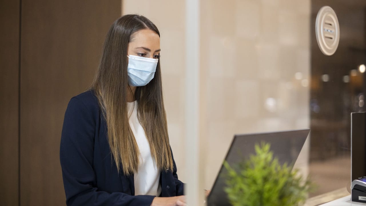 Front Desk Agent with Face Mask Working Behind Safety Glass Close Up
