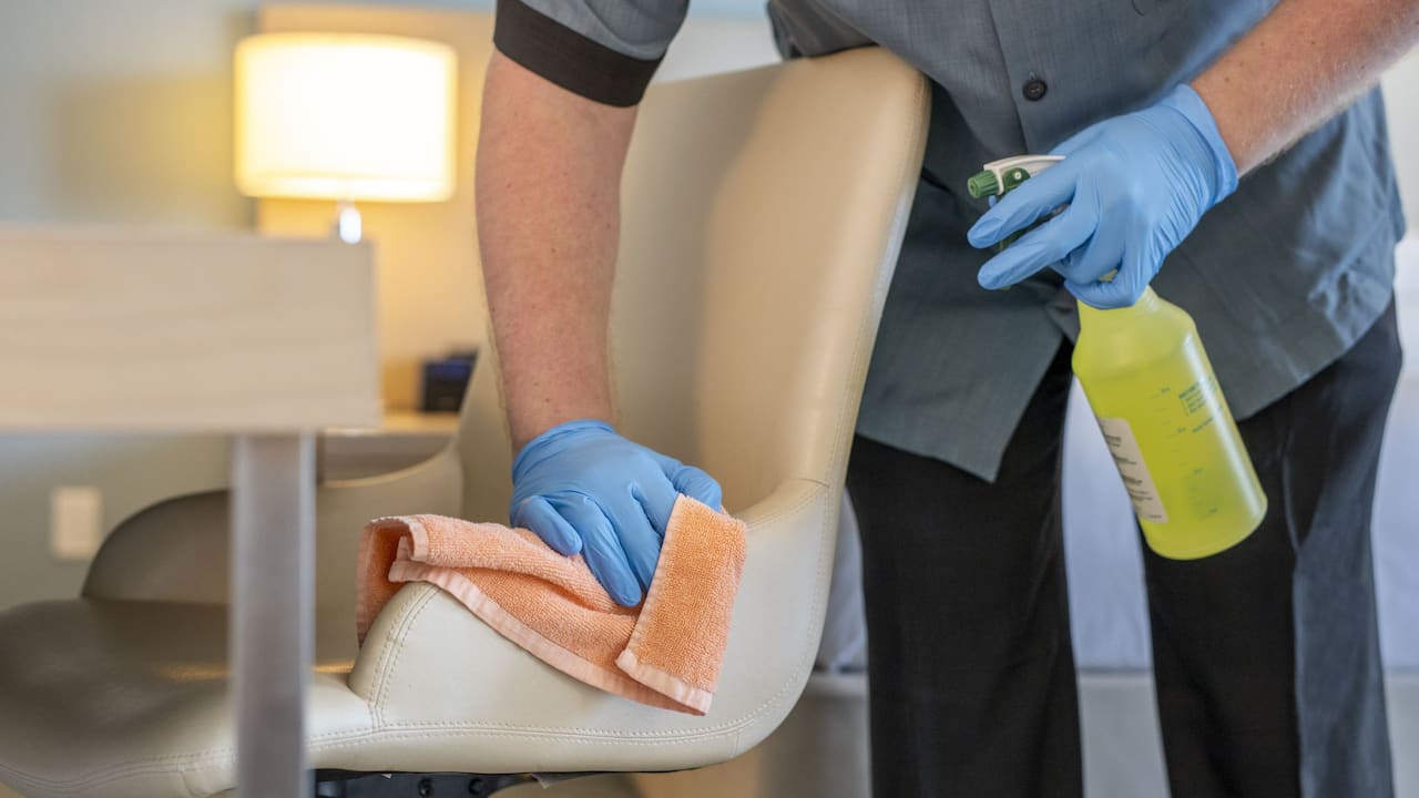 Employee with Gloves PPE Wiping Down Guest Room Desk Chair
