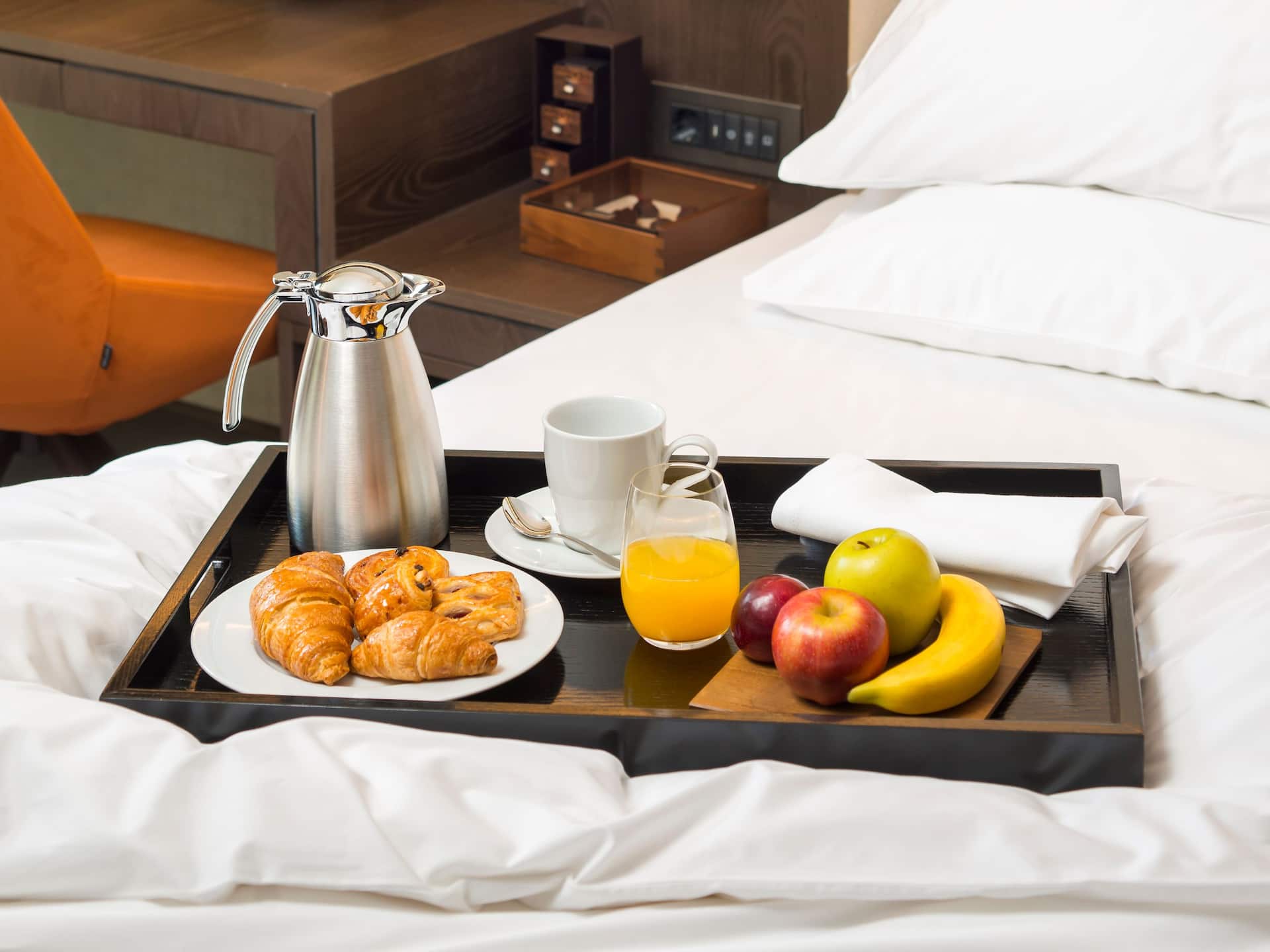 A cozy in-room dining setup at Hyatt Regency Sofia featuring a breakfast tray with freshly baked pastries, fruits, orange juice, and coffee, served on a plush bed for a relaxing start to the day.