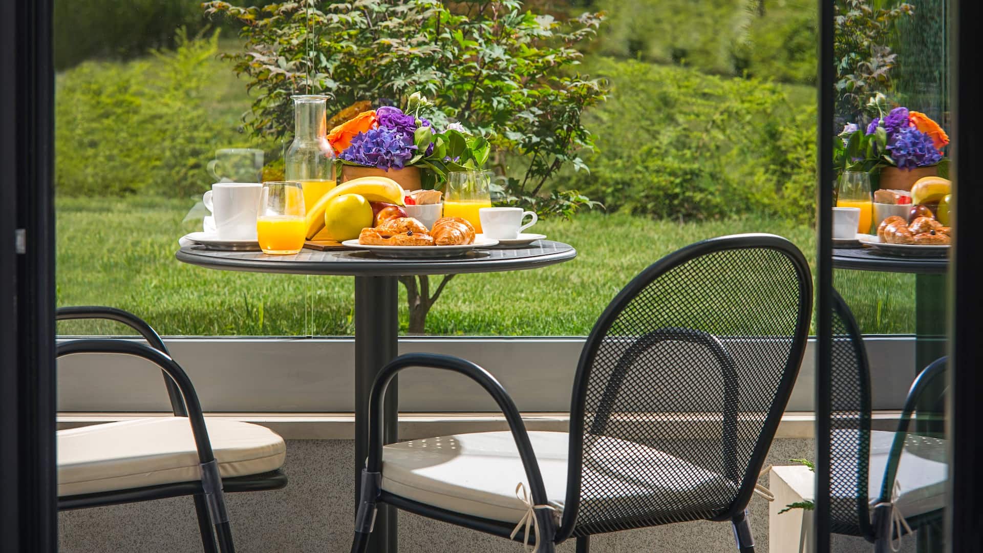 1 из 2 Serene King Bed Garden View room terrace at Hyatt Regency Sofia, featuring an intimate outdoor seating area with a lush green backdrop, fresh breakfast spread, and vibrant floral arrangement.